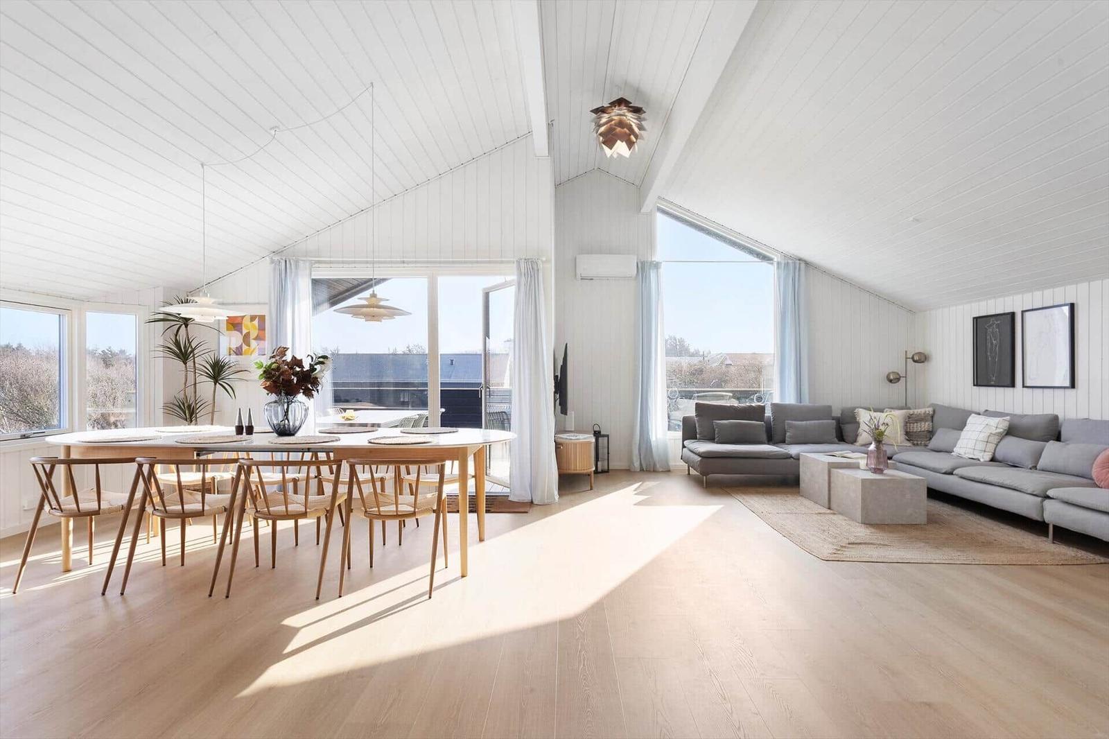 Living and dining area with wooden floor, large sofa, and dining set under high ceiling.