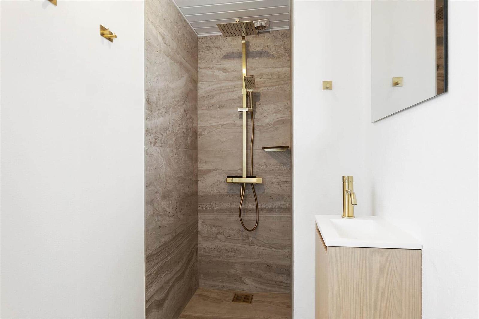 Shower with gold fixtures and stone wall. Sink with gold faucet.