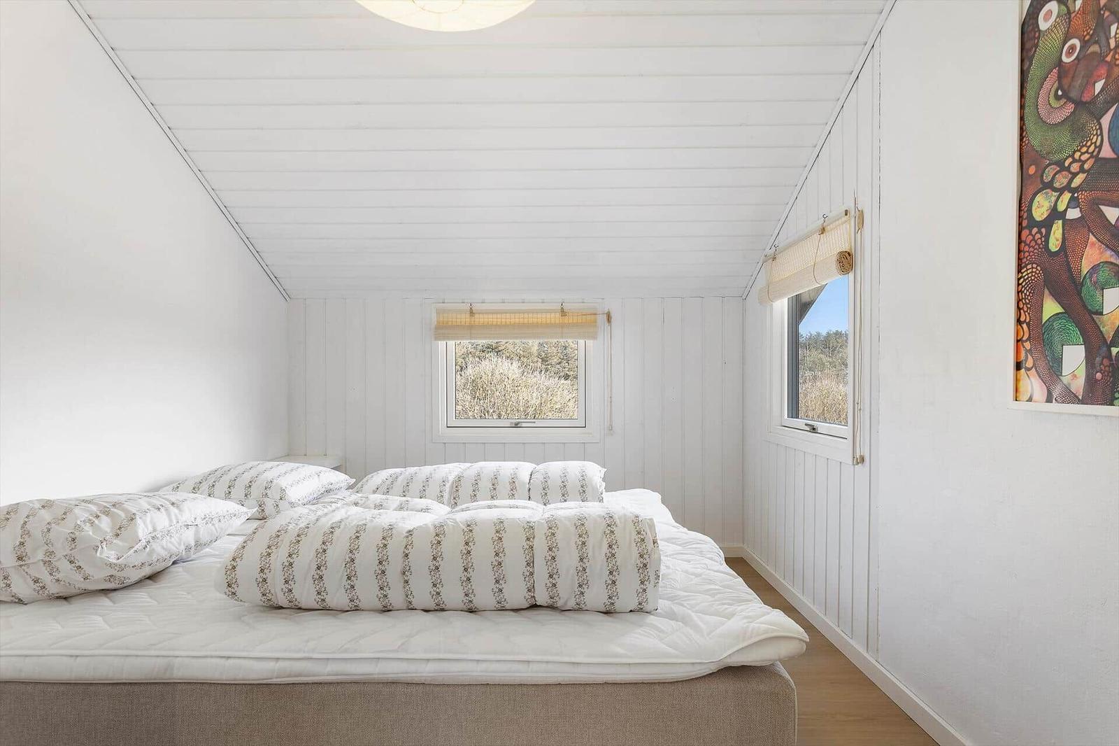 Bedroom with bed, windows, and wall art.