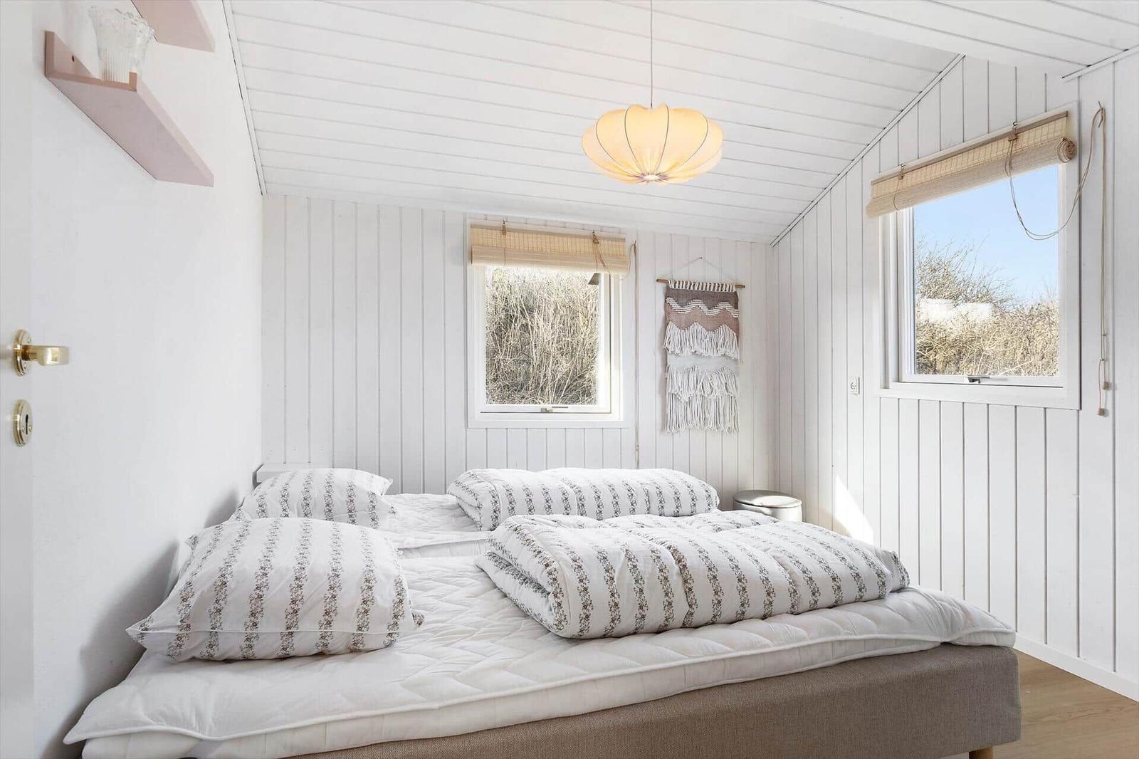 Bedroom with bed, windows, and ceiling lamp.