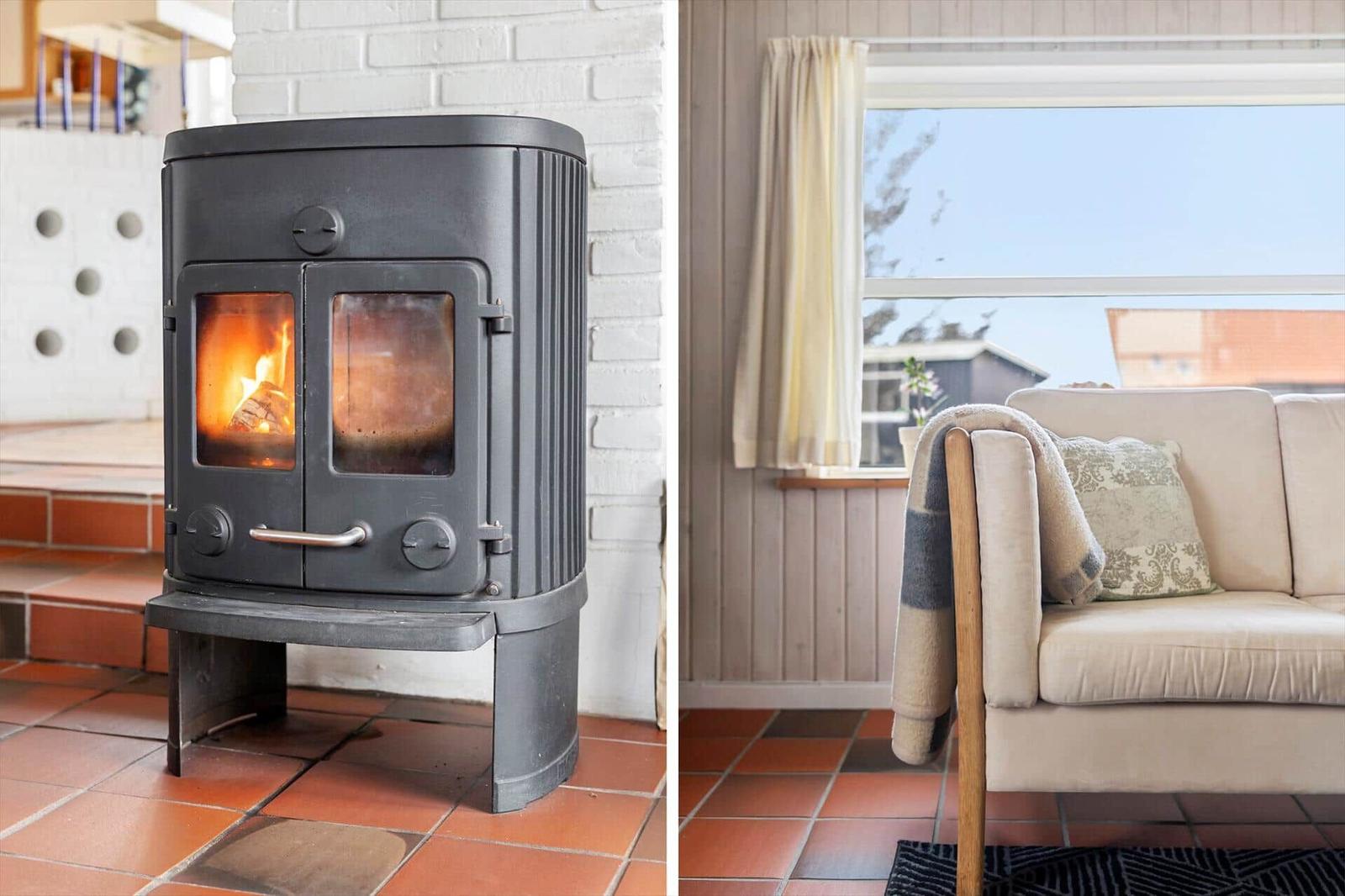 Wood-burning stove and sofa with cushions and blanket by window.