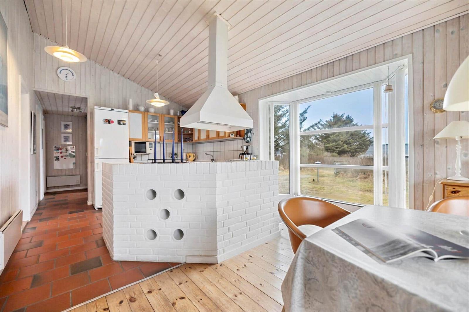 Kitchen with white cabinets and brick island. Wooden floor and large windows.