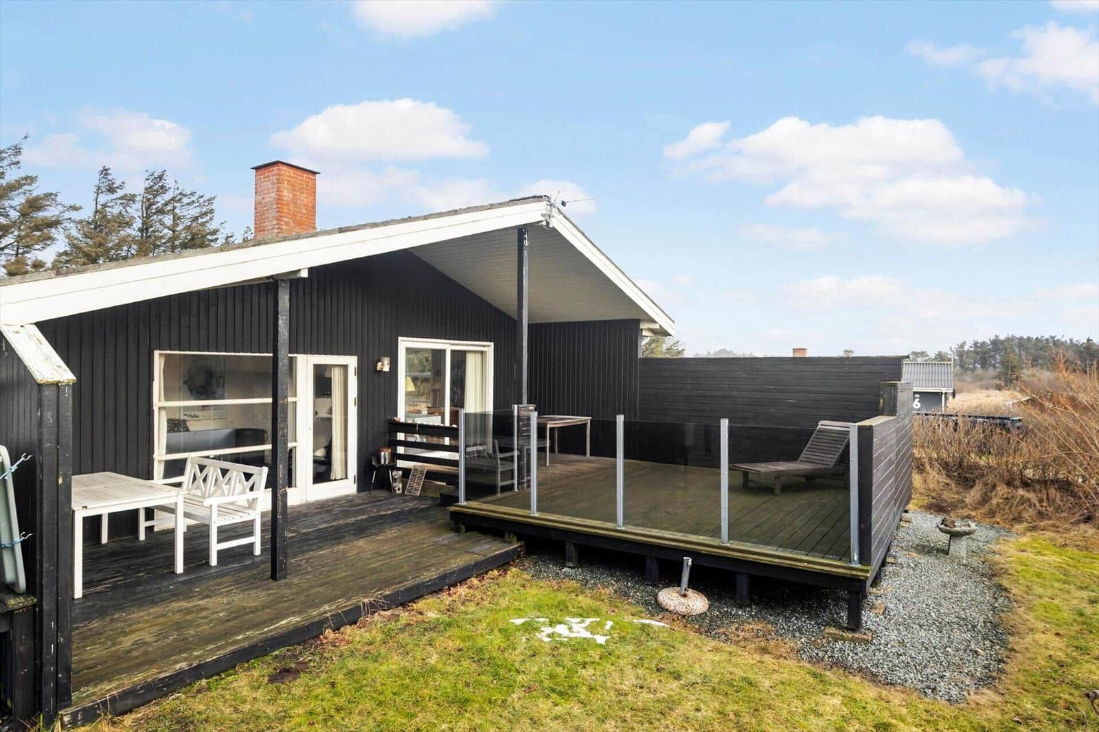 Black house with terrace and garden. White garden furniture and wooden decks.