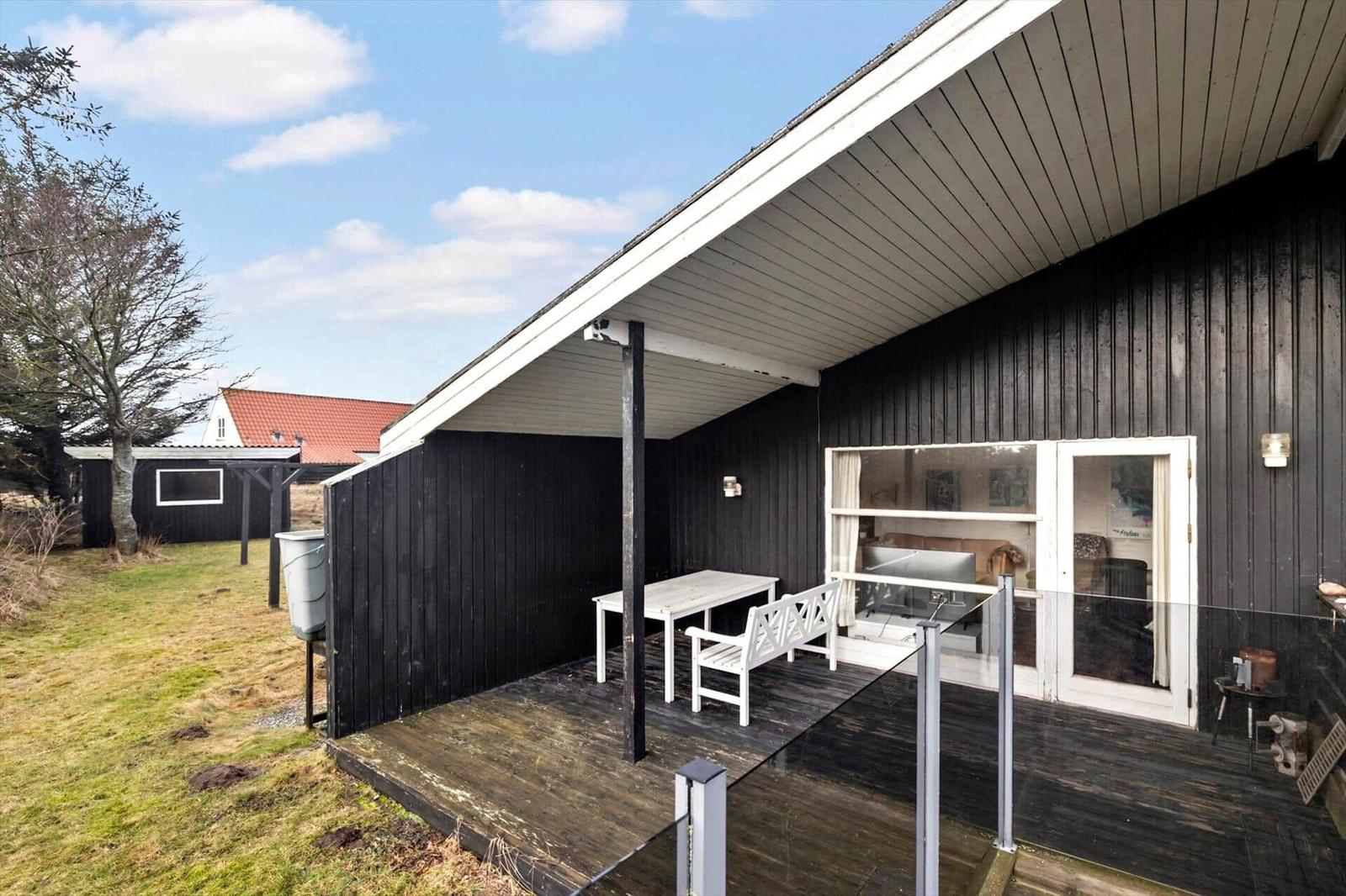 Deck with table and chairs beside black wooden house under blue sky.