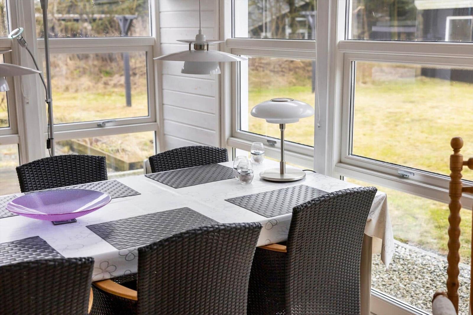 Dining table with chairs and tablecloth by large windows.