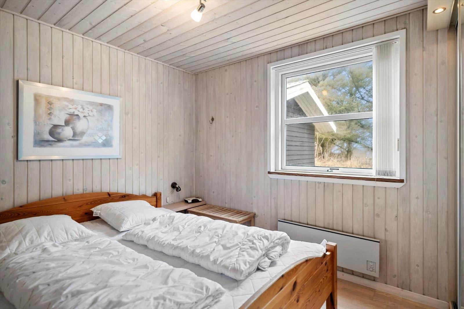 Bedroom with wooden paneling, bed, window, and wall art.