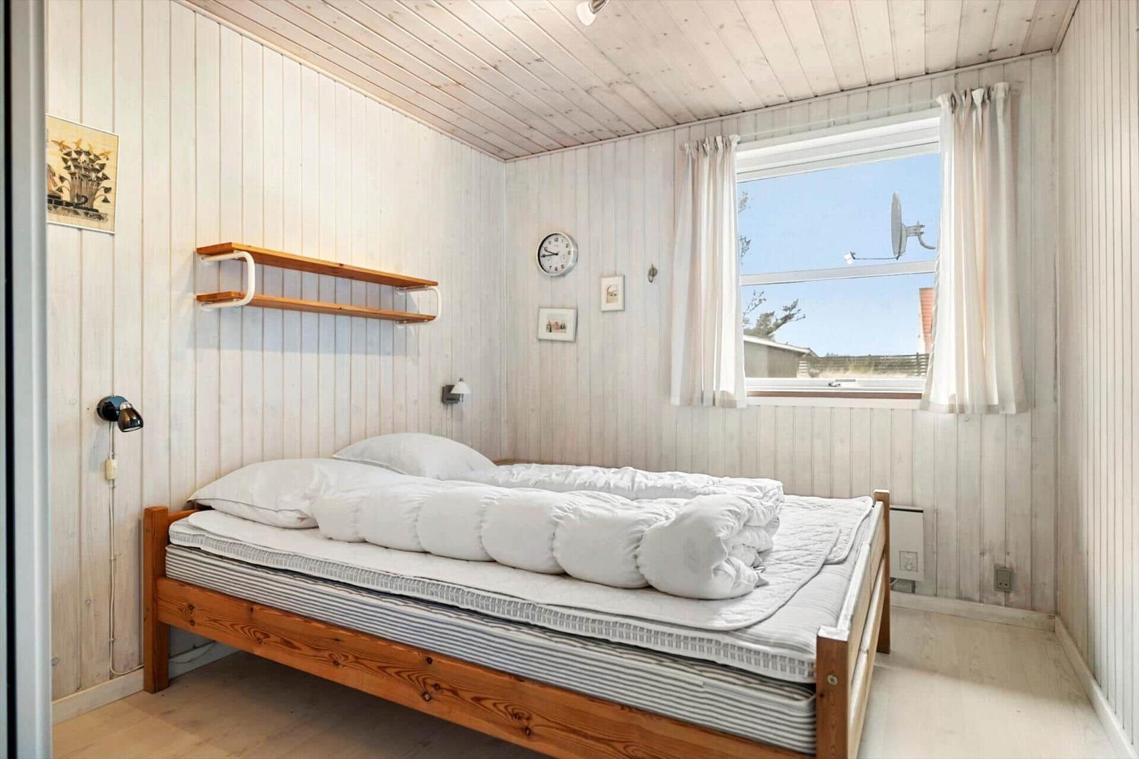 Bedroom with wooden bed, window, and wall shelf.