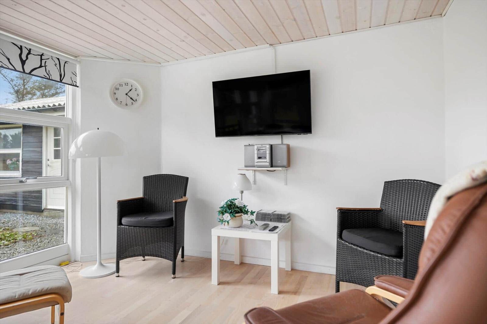 Living room with TV, two chairs and table. Wooden ceiling and window with view.