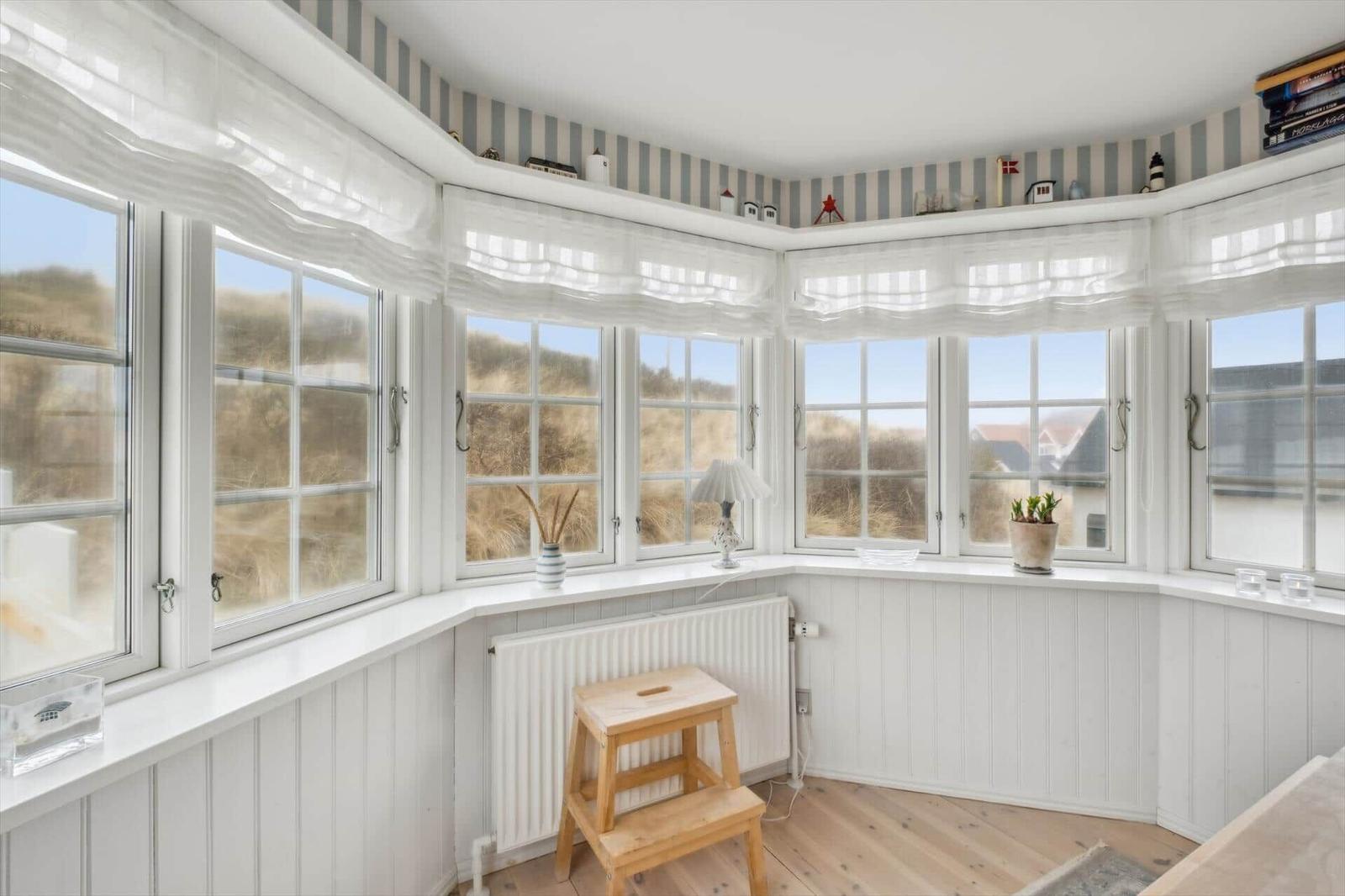 Room with bay windows, white walls, and wooden floor. Plants and decor are on the windowsill.