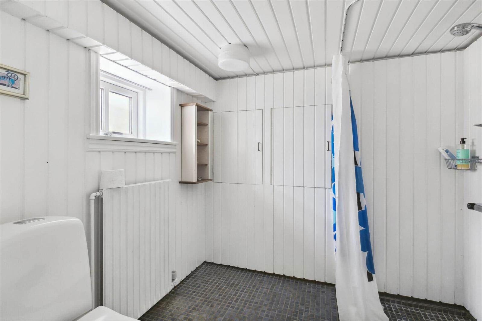 Bathroom with shower, toilet, and window. White walls and floor tiles.