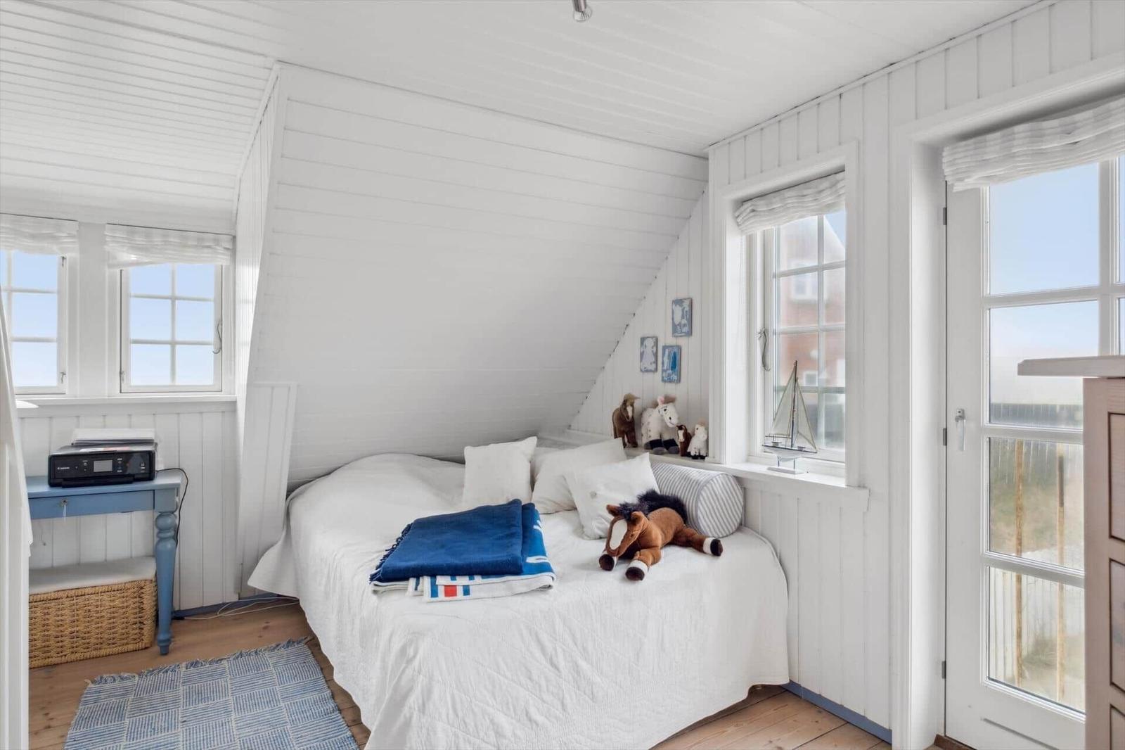 Bedroom with white wood walls, bed, windows, and toys.