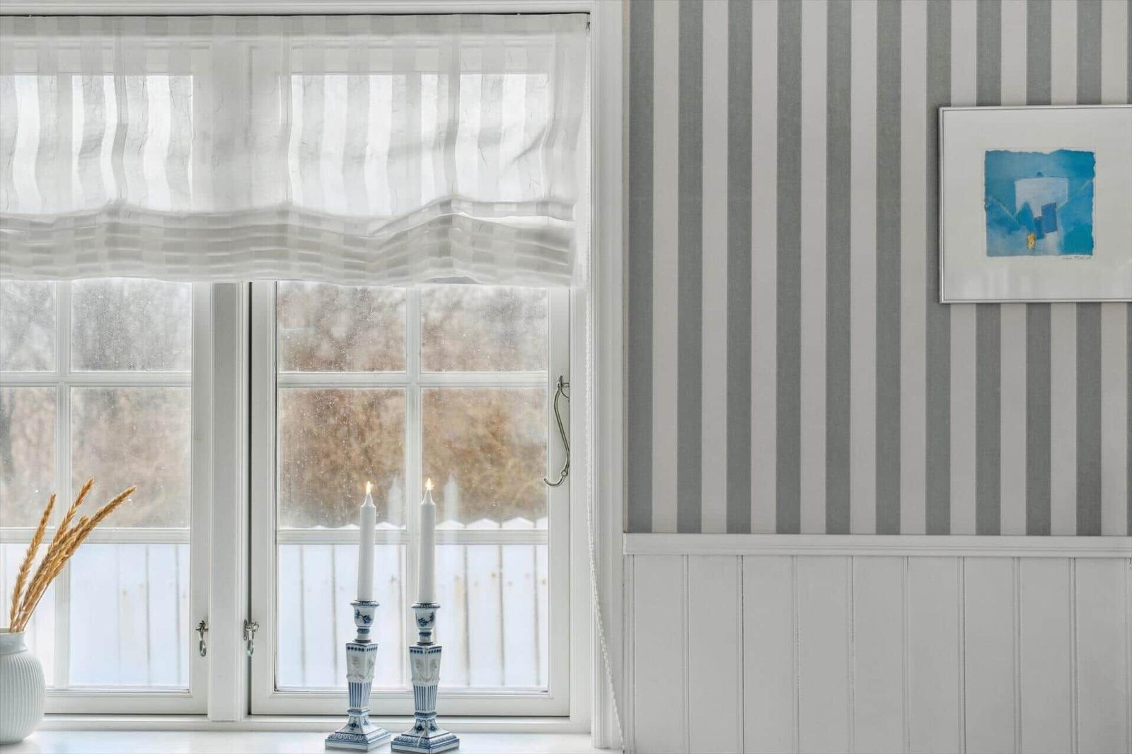 Window with sheer curtains, two lit candles, and striped wall.