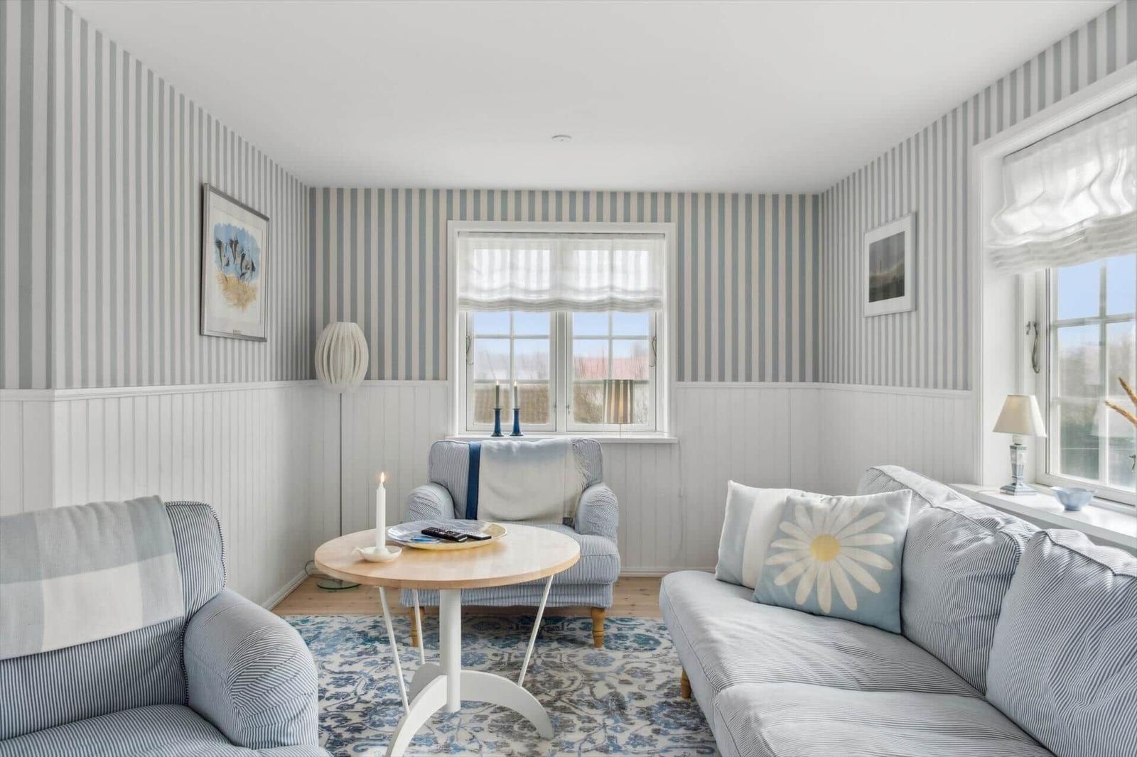 Living room with striped walls, sofa and chair. Windows with roller blinds and rug.