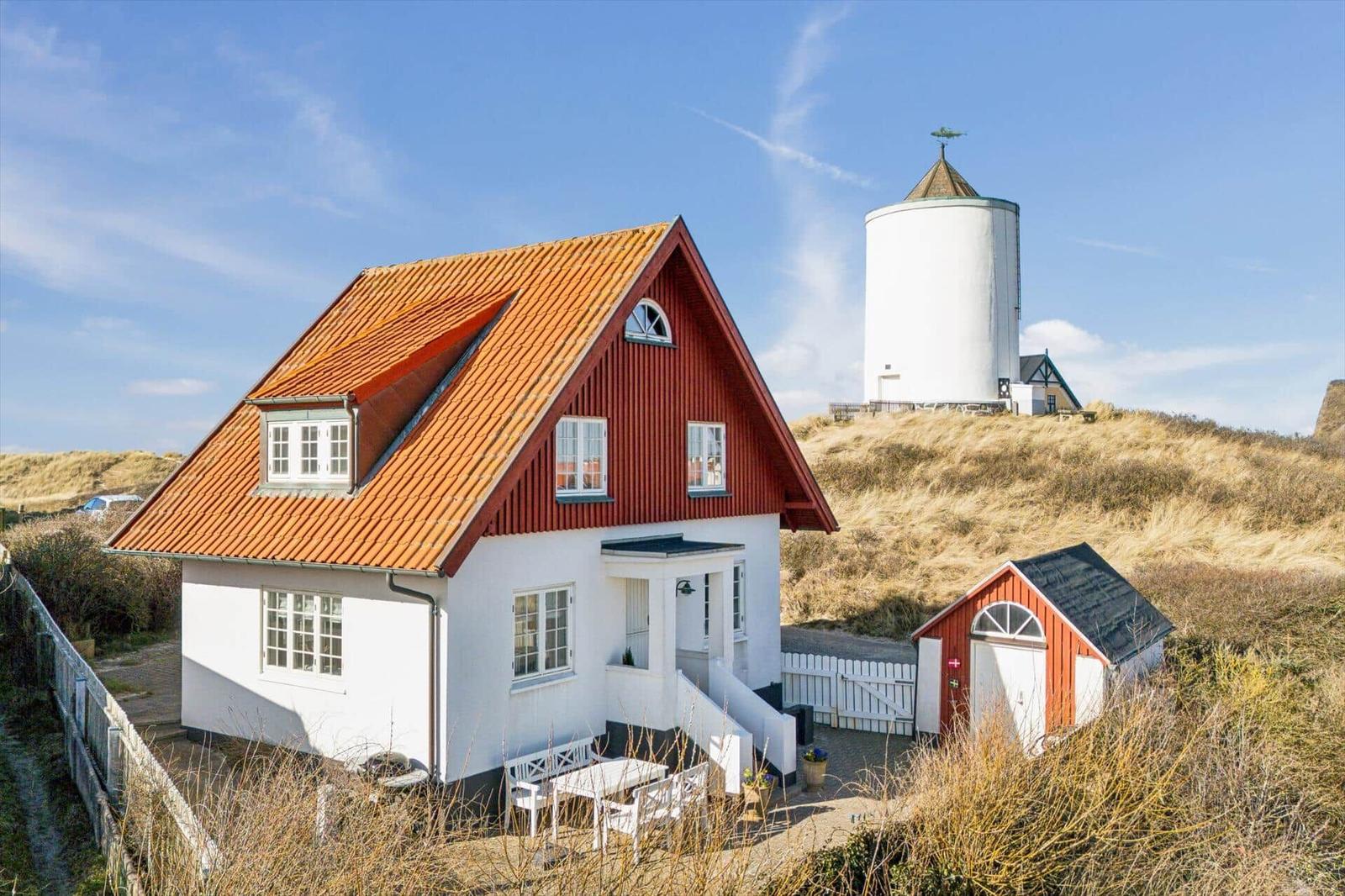 A red house with white lower section and orange roof. Behind it stands a white windmill structure.