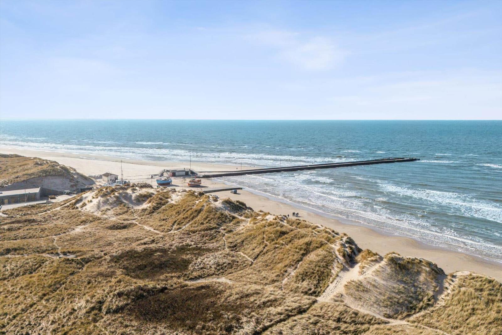 Beach with dunes, boathouses, and pier. View of the sea.