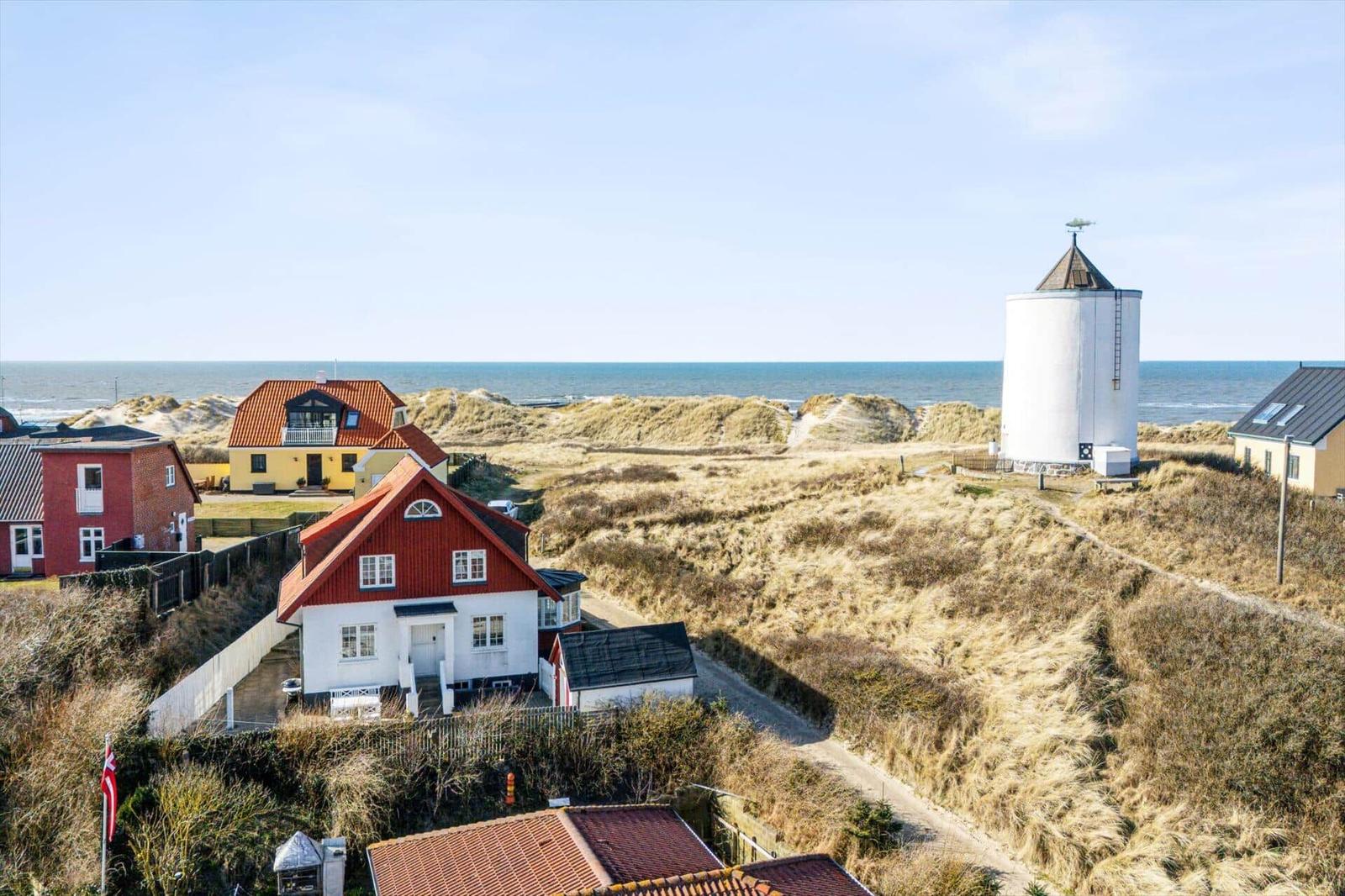 House with red roof, white facade, and view of the sea and a windmill.