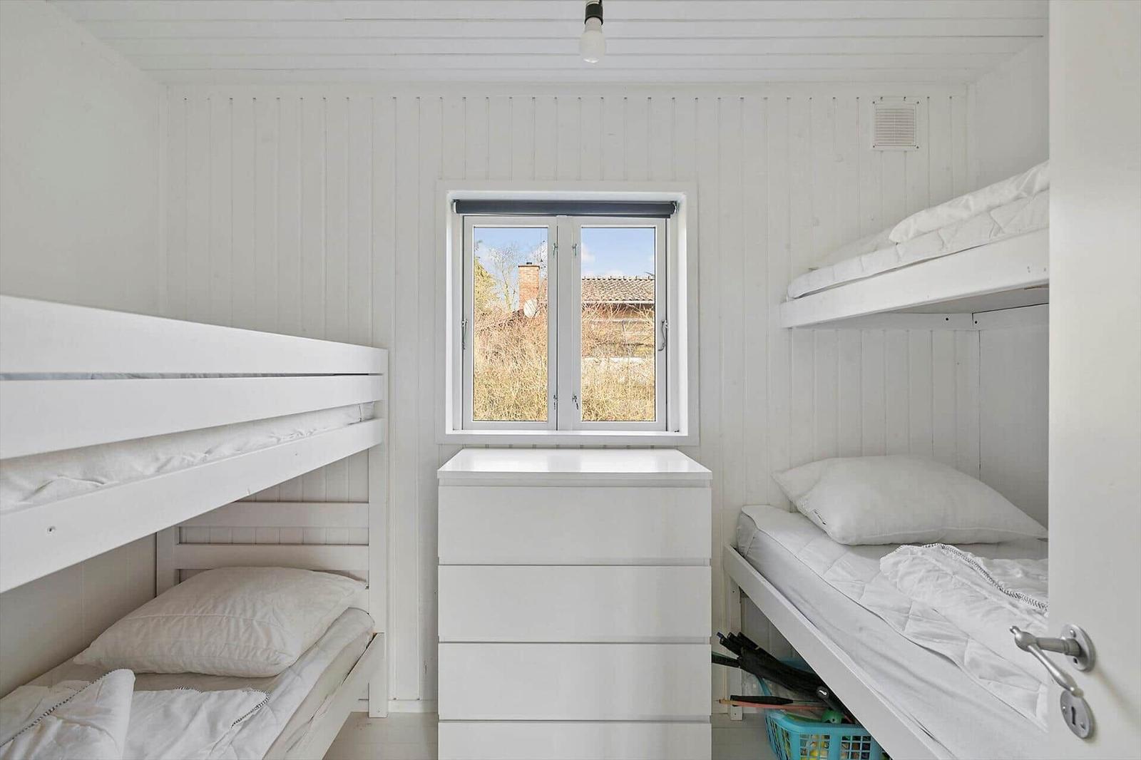 Room with two bunk beds, white dresser, and window with outdoor view.