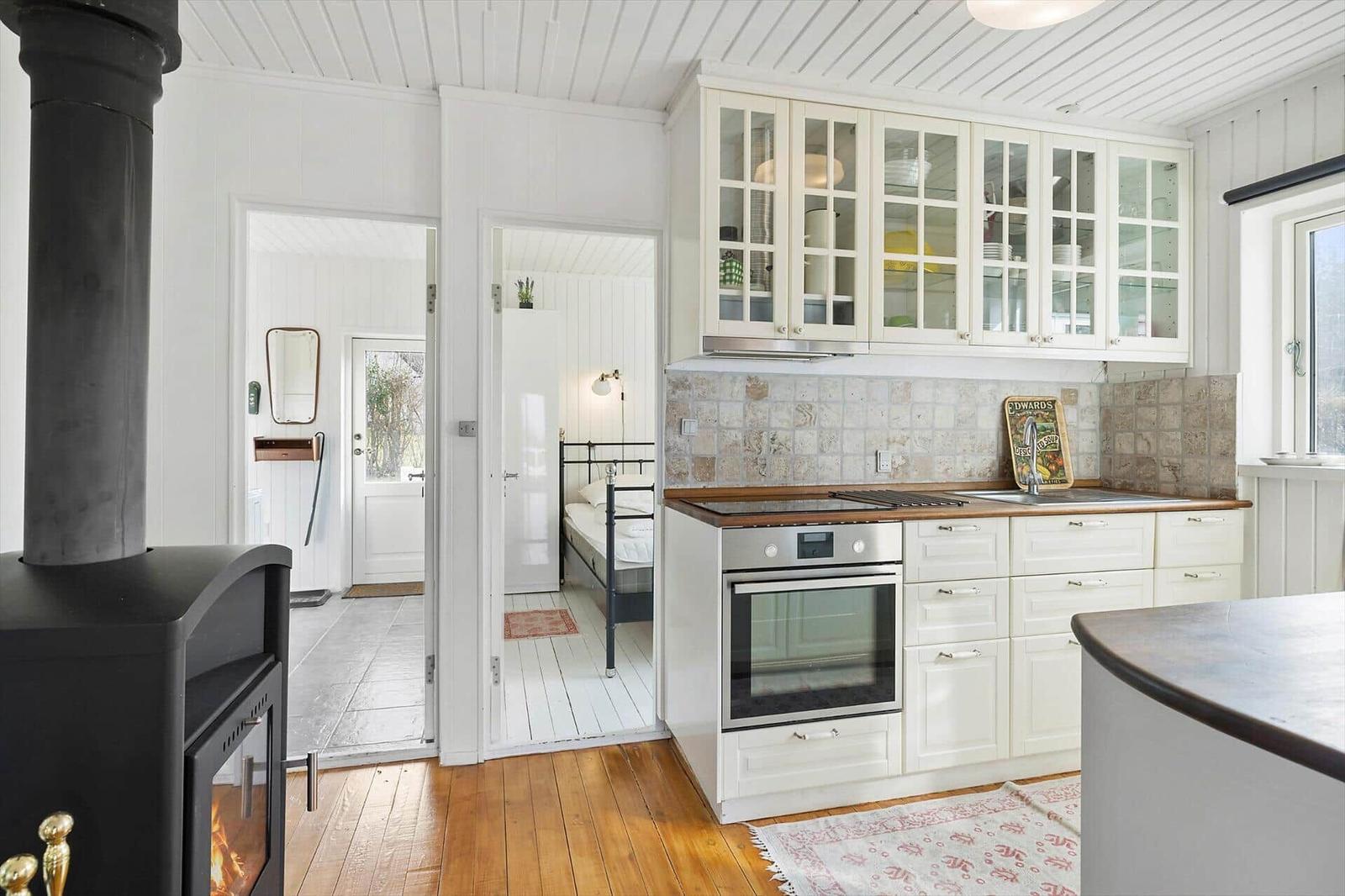 Kitchen with white cabinets, stone backsplash, and wooden floor. Bedroom visible in background.