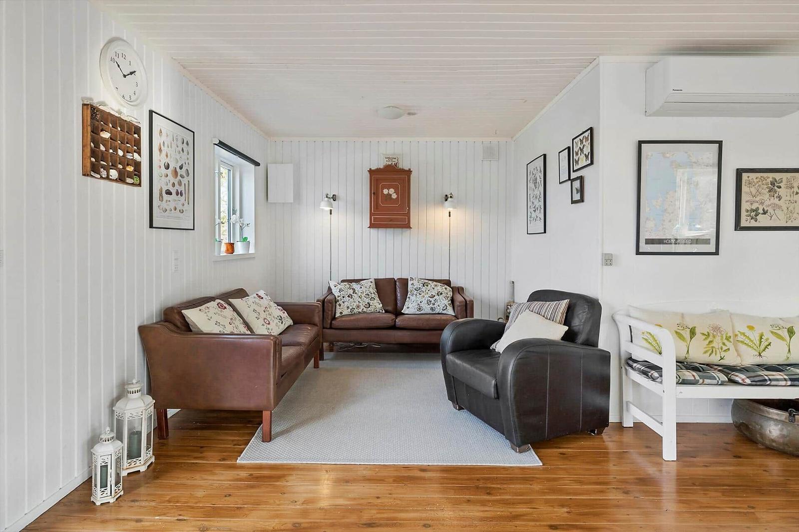 Living room with brown leather sofas, wooden floor, and white walls with pictures.