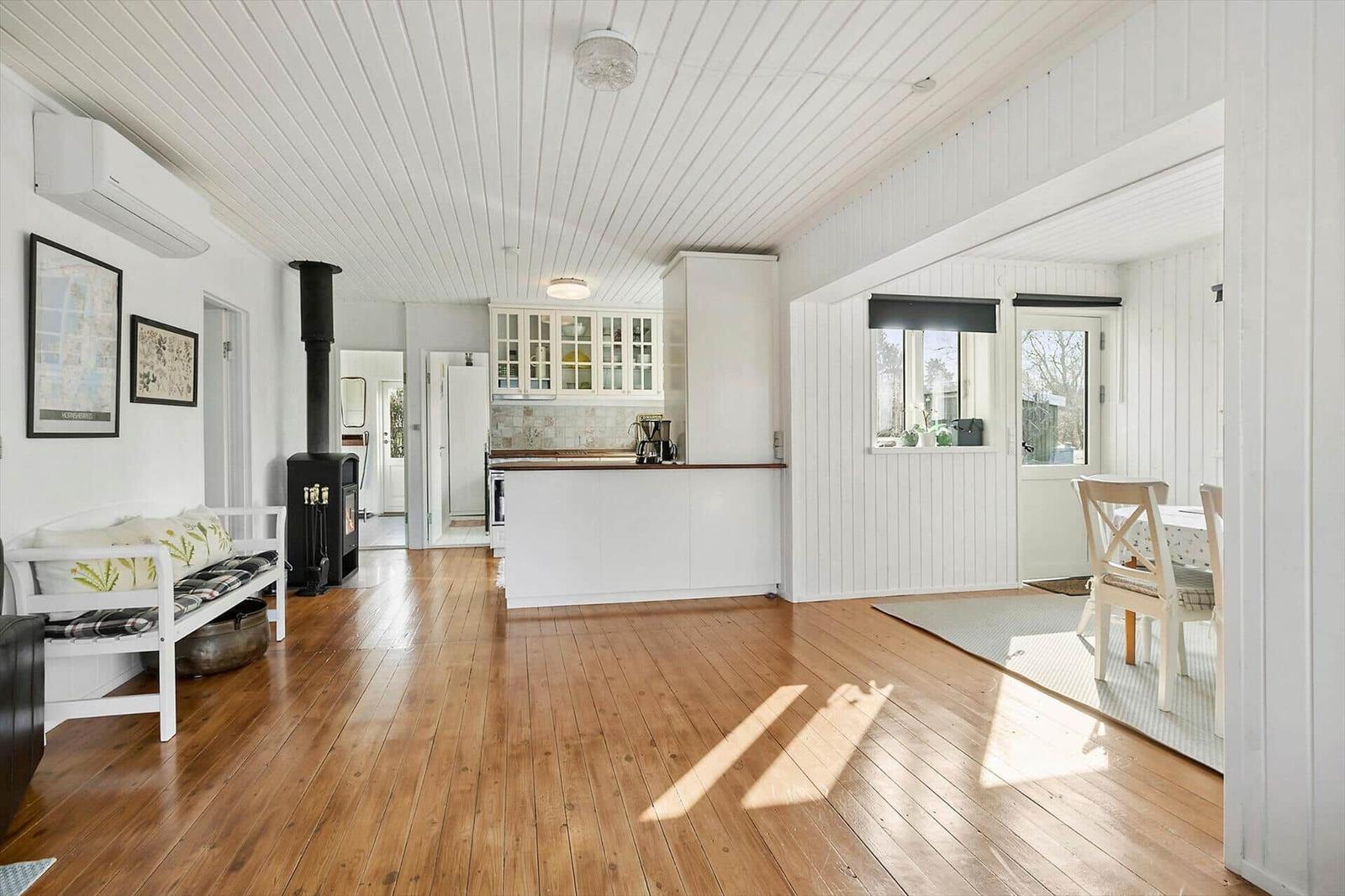 Living kitchen with wooden floor, white walls, and wood stove.