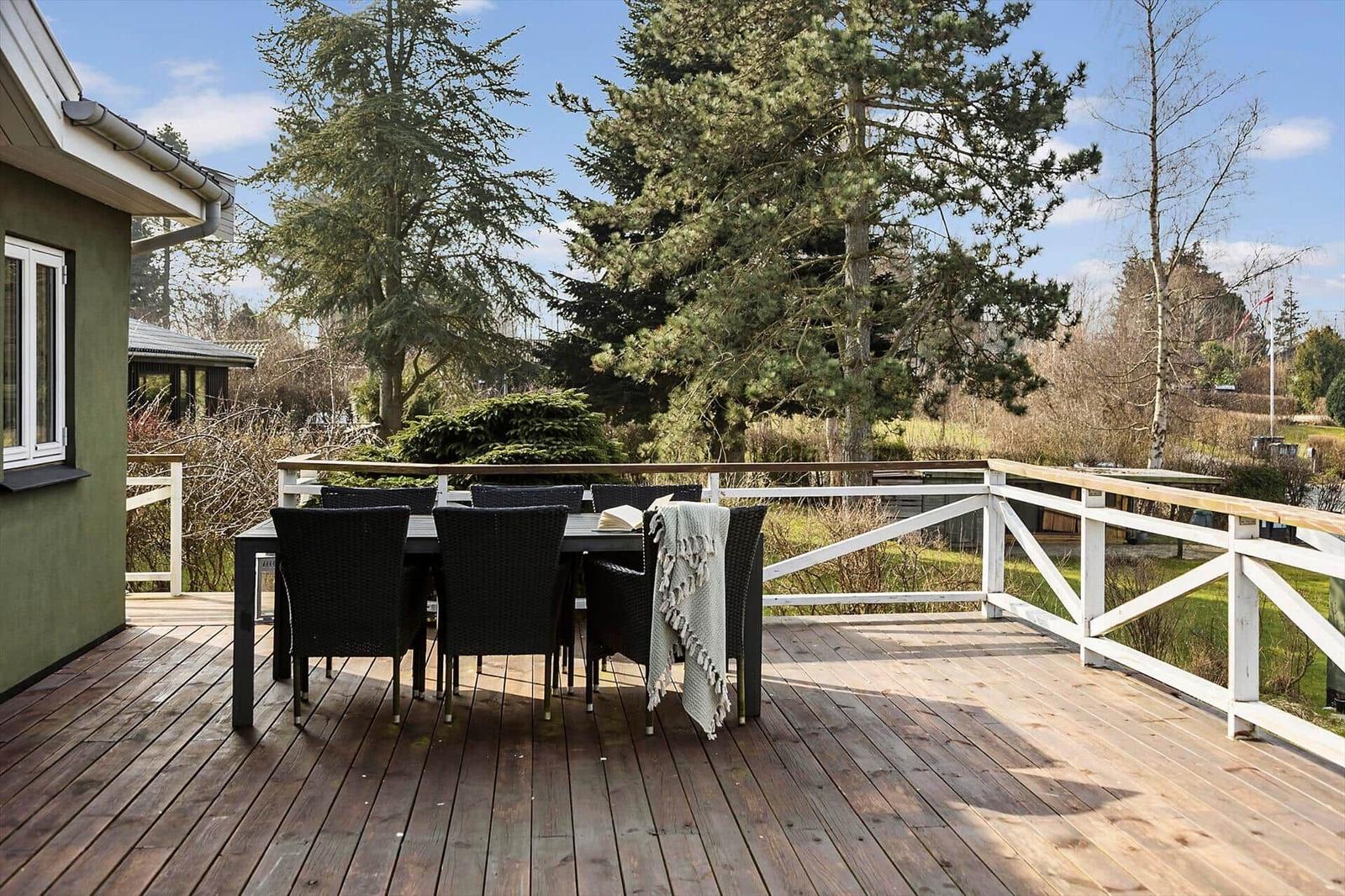 Deck with dining table and chairs, surrounded by trees and greenery.
