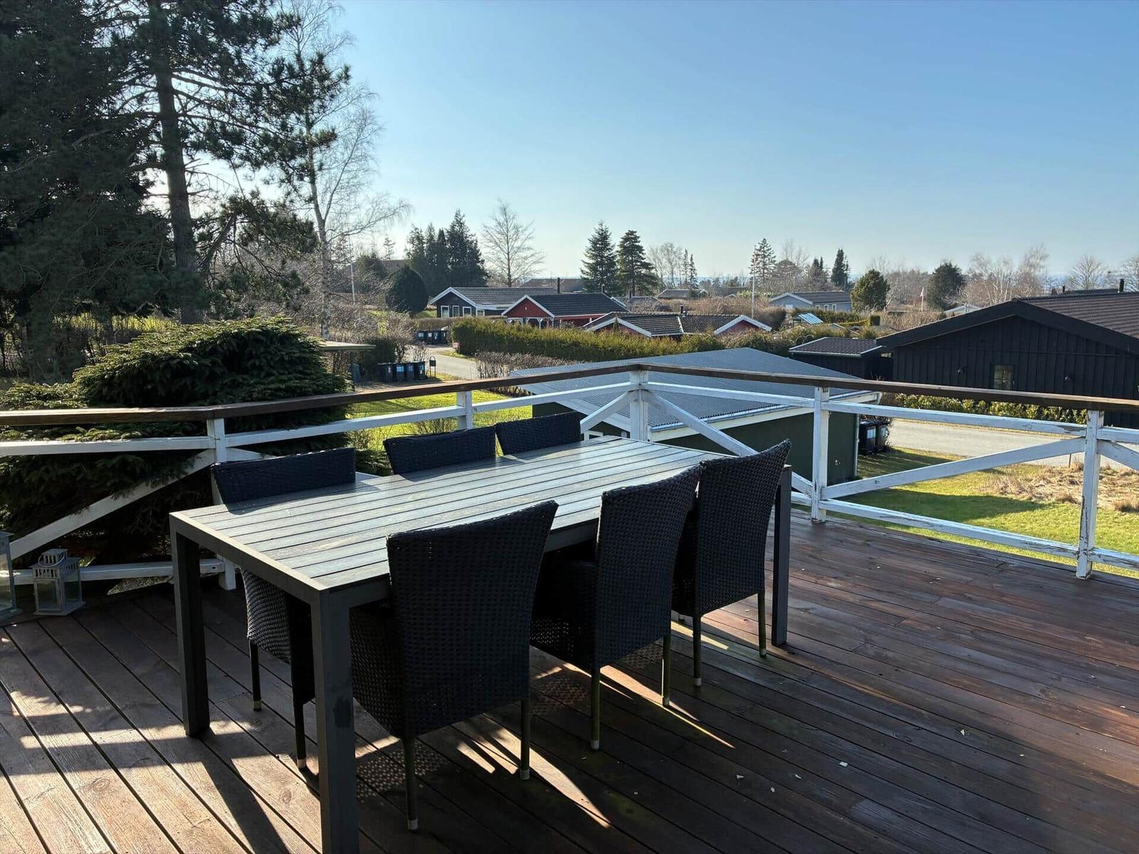 Deck with table and chairs, view of houses and trees.