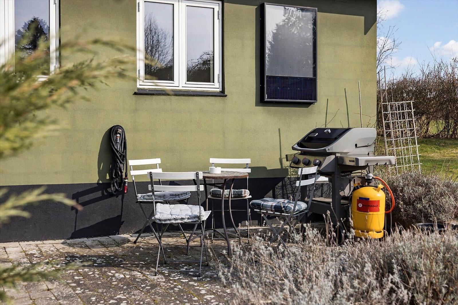 Terrace with table, chairs, and grill against house wall.