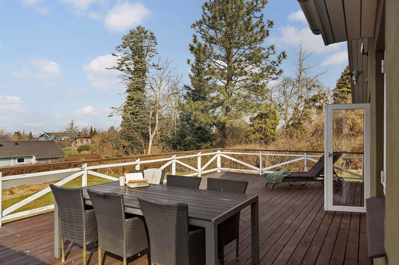 Deck with table, chairs, and lounge chair. View of trees and holiday home.