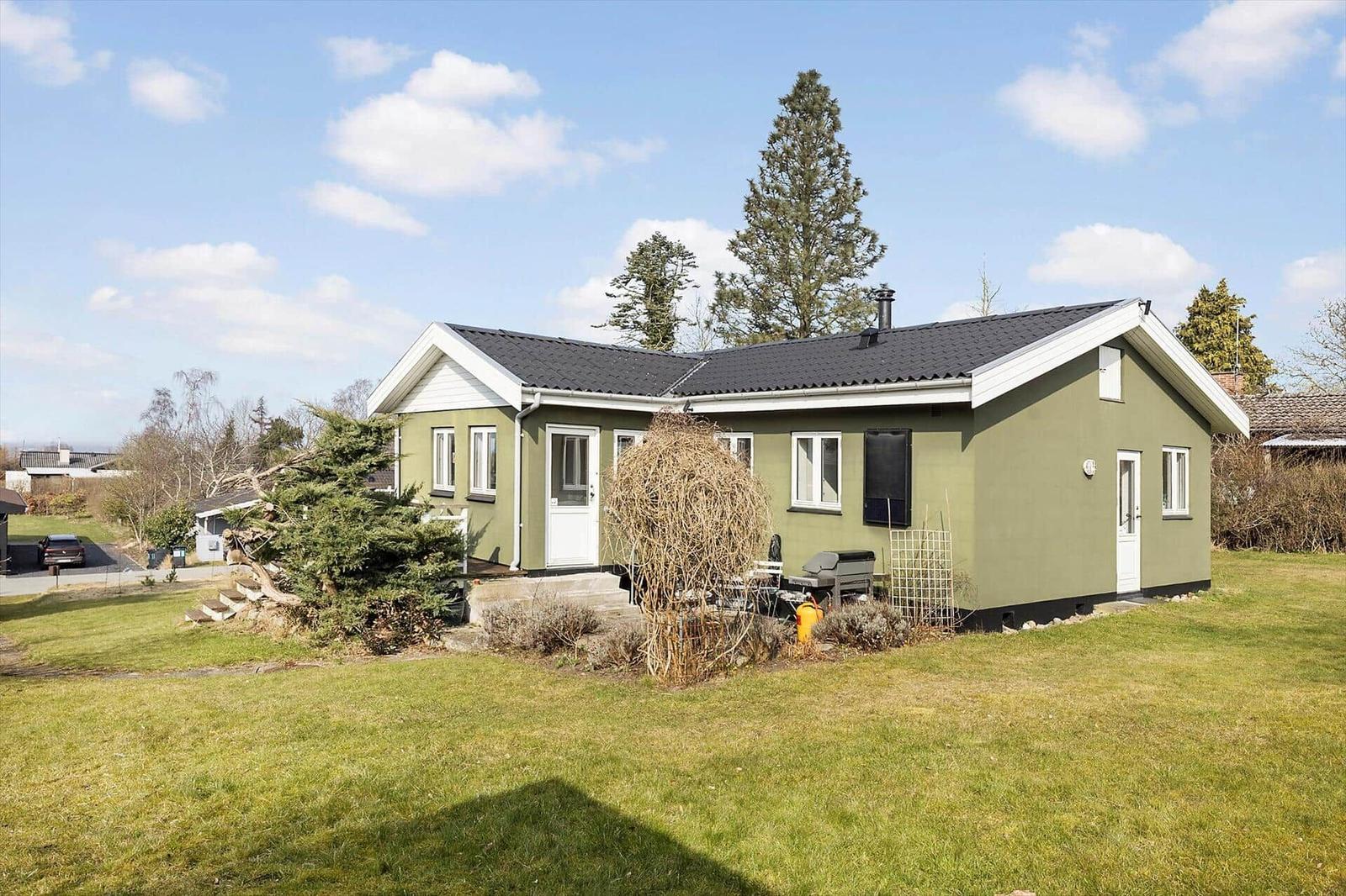 Green house with garden and grill area under blue sky.