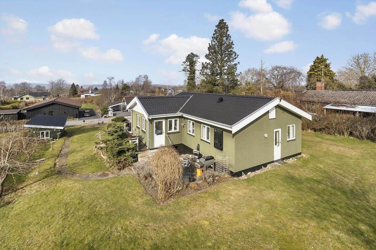 Green house with garden and grill area under blue sky.