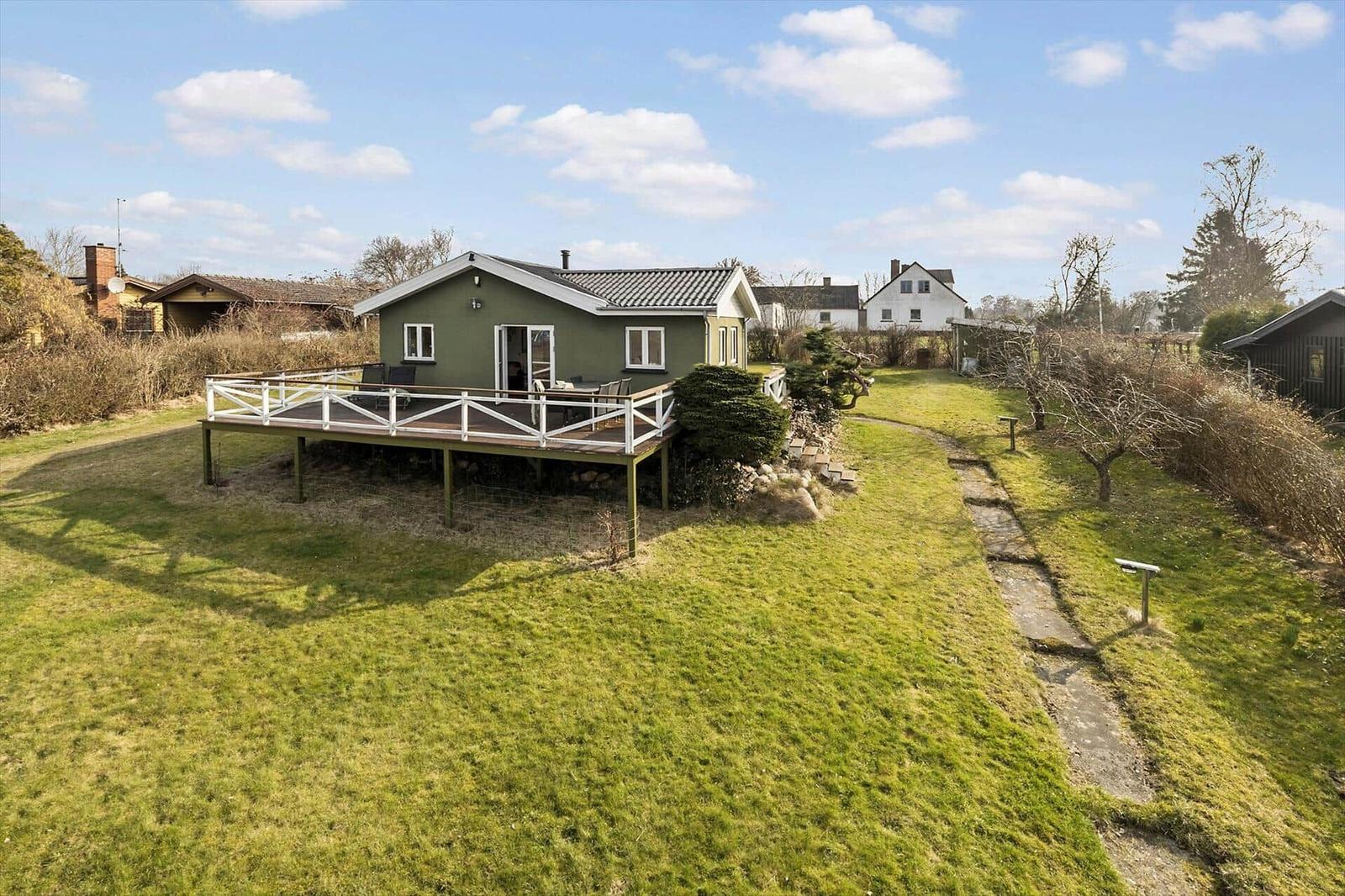 Green house with terrace and garden. Background: other houses and trees.