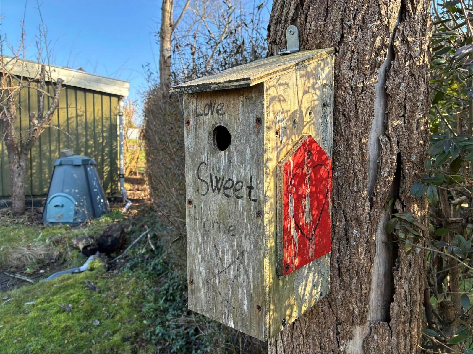 Wooden birdhouse on tree with inscription Love Sweet Home and red heart