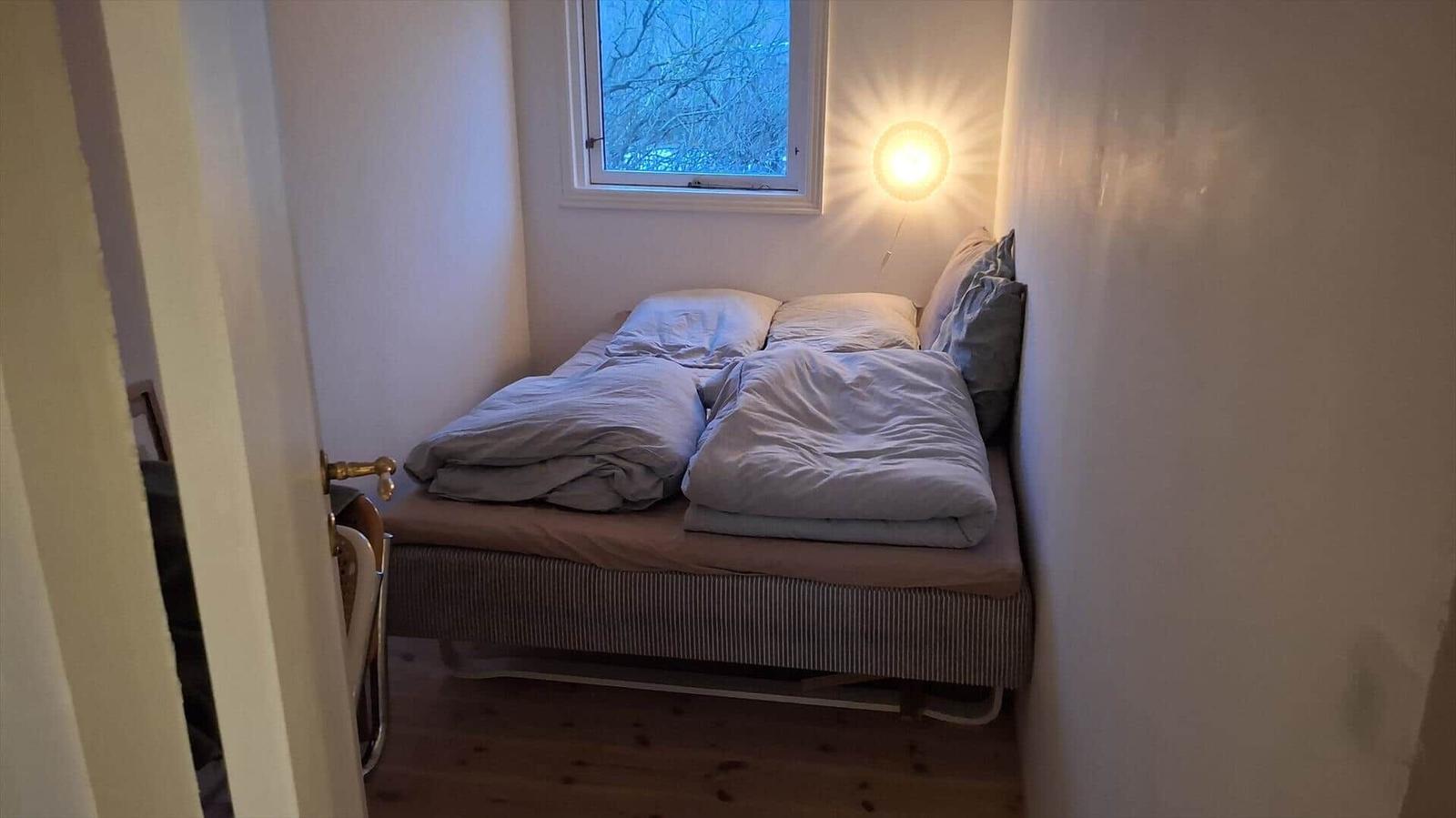 Schlafzimmer mit Bett, Fenster und Wandlampe.