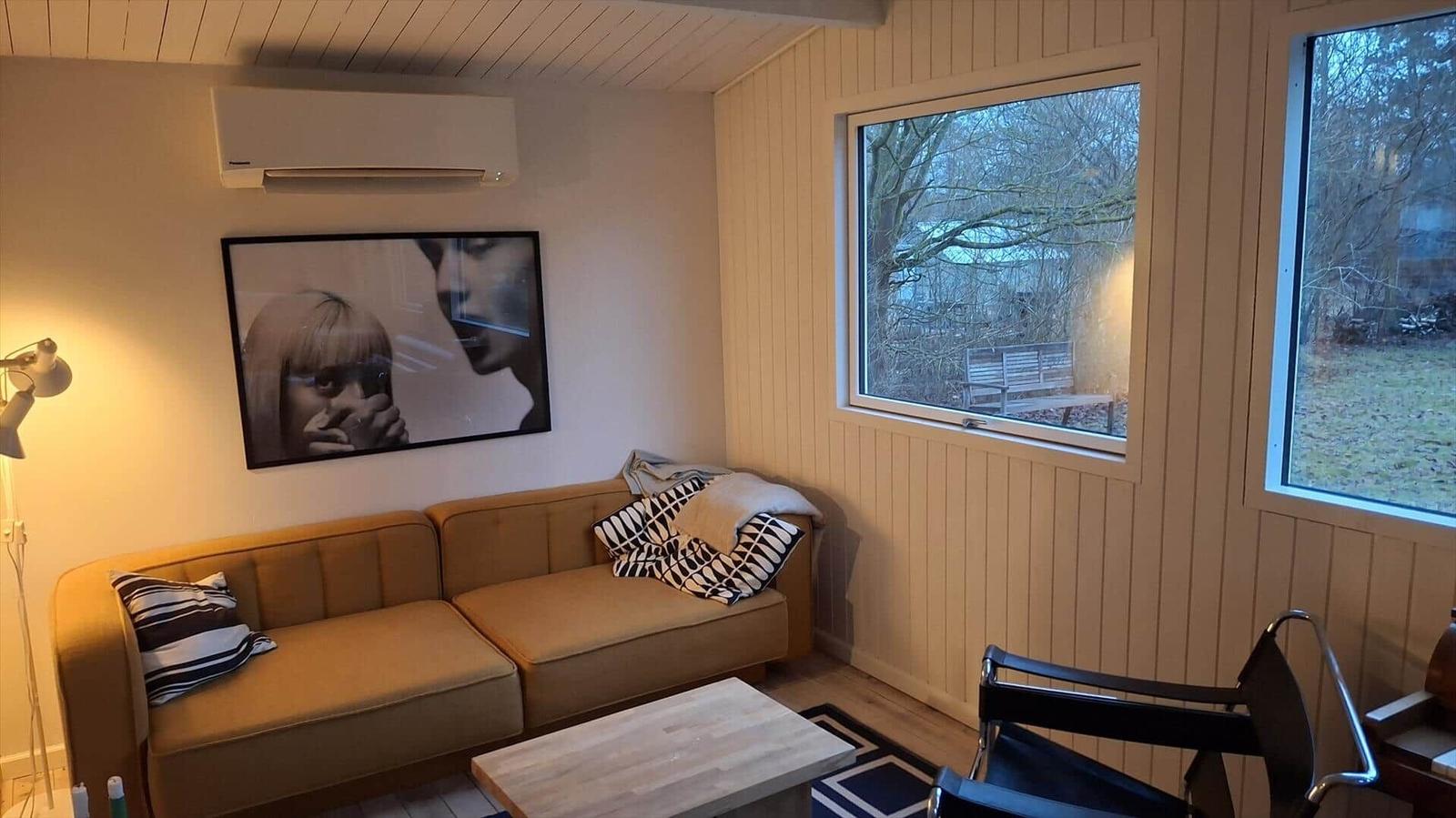 Wohnzimmer mit Sofa, Tisch und Fenstern zur Außenseite.