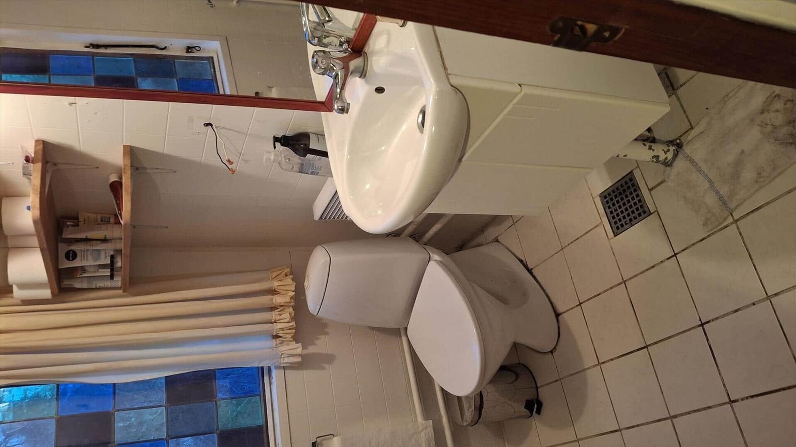 Badezimmer mit Toilette, Waschbecken und Fenster mit bunten Fliesen.