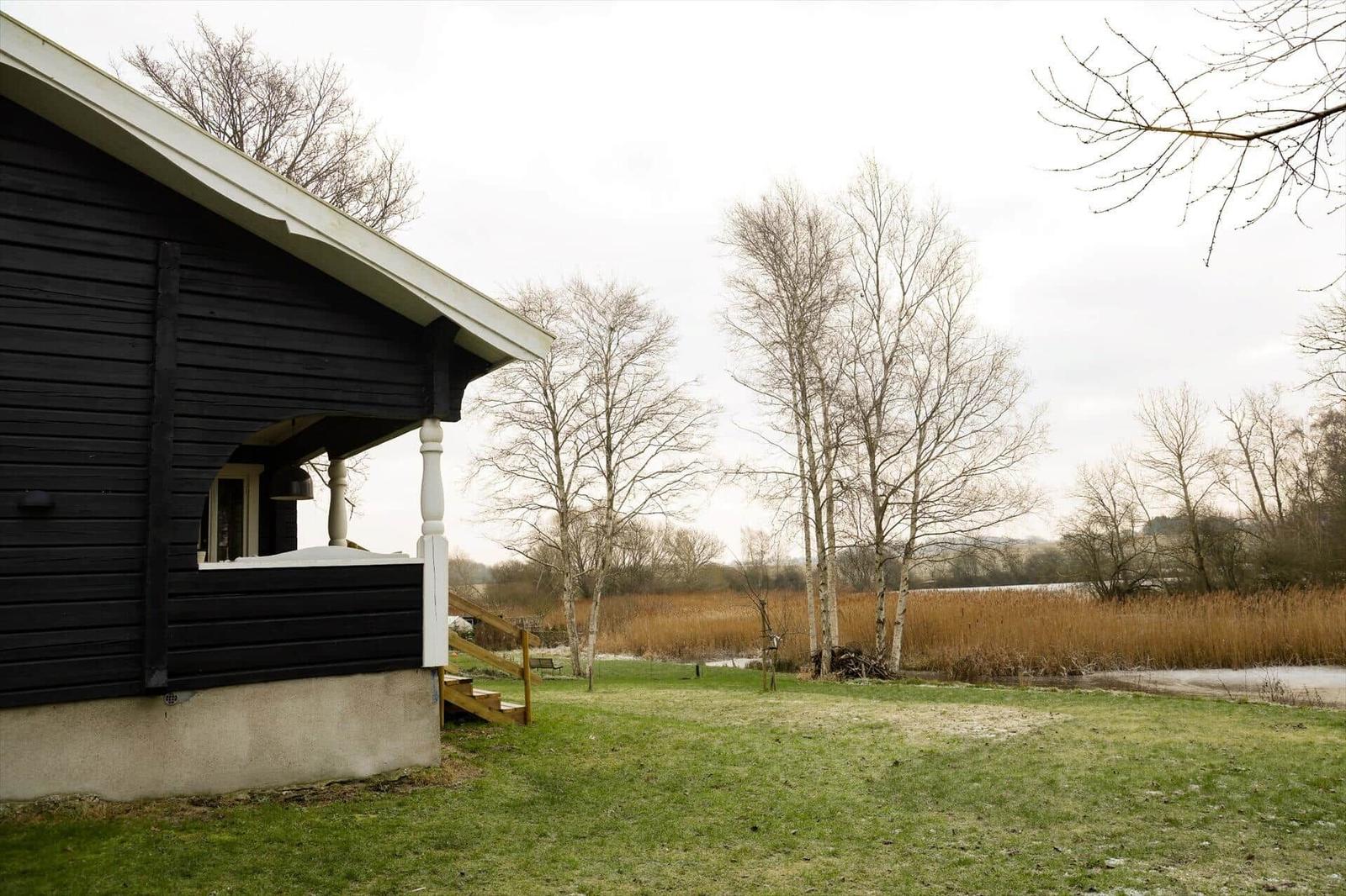 Schwarze Holzhütte mit Veranda, Grasfläche und Bäumen im Hintergrund.