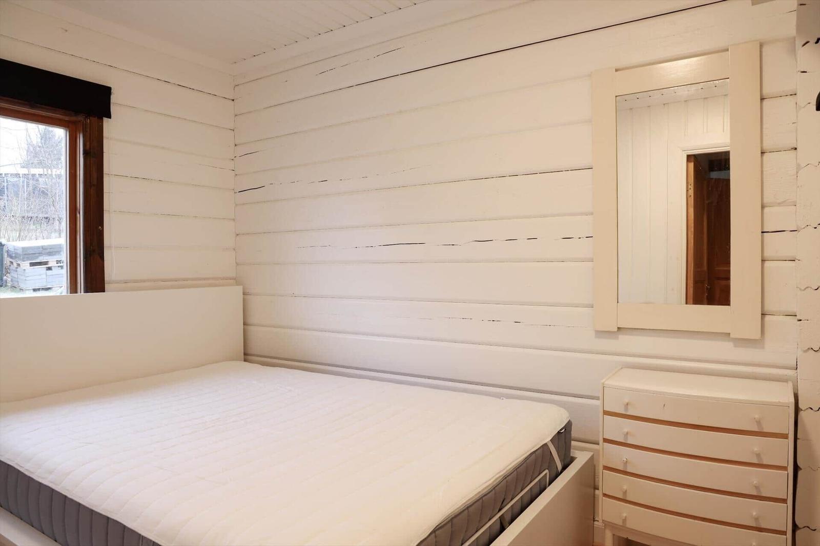 Schlafzimmer mit Bett, Schrank und Spiegel an weiß verputzten Wänden.