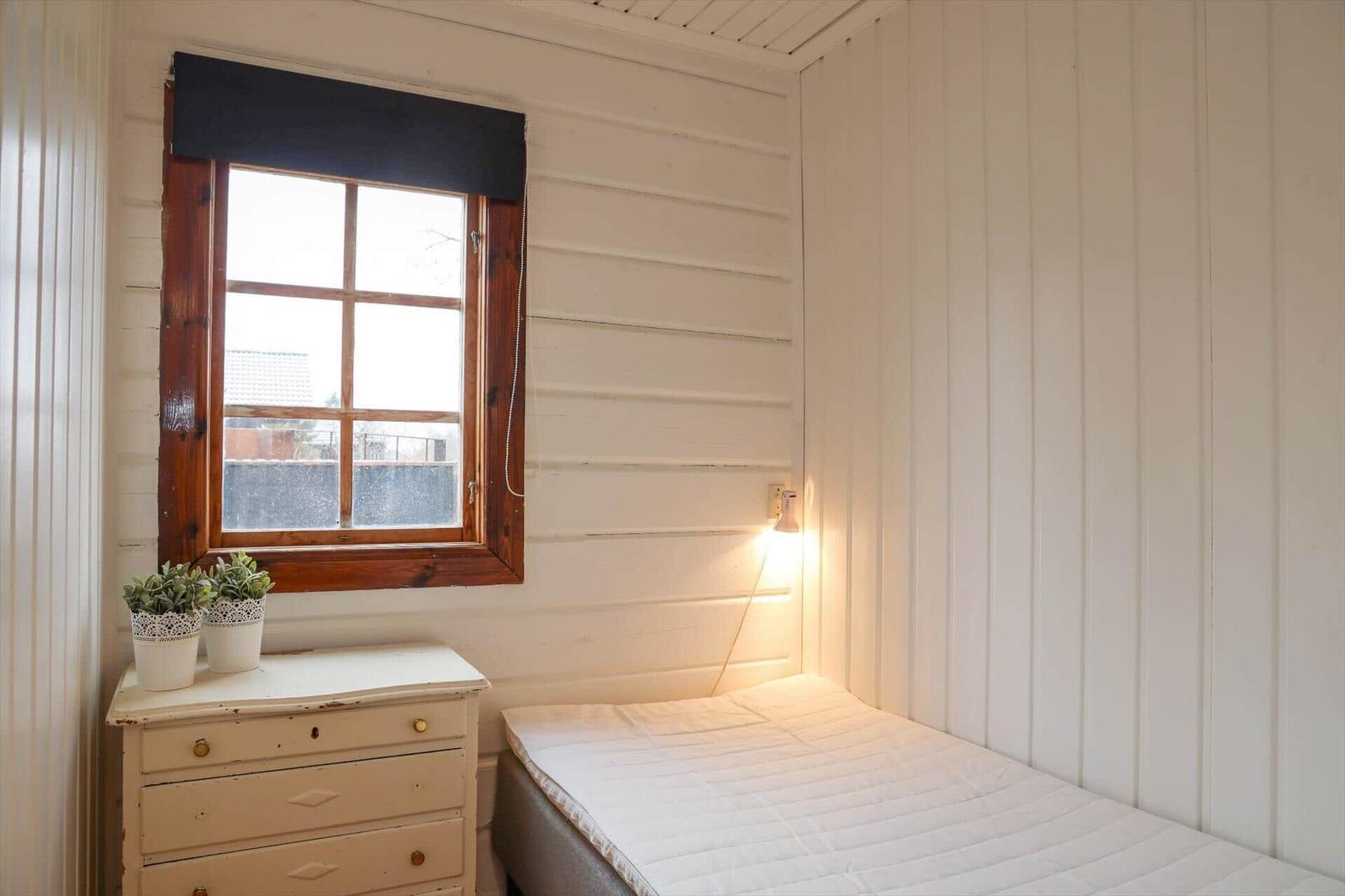 Ein Schlafzimmer mit weißer Wandverkleidung, einem Bett, einem Schrank und einem Fenster.