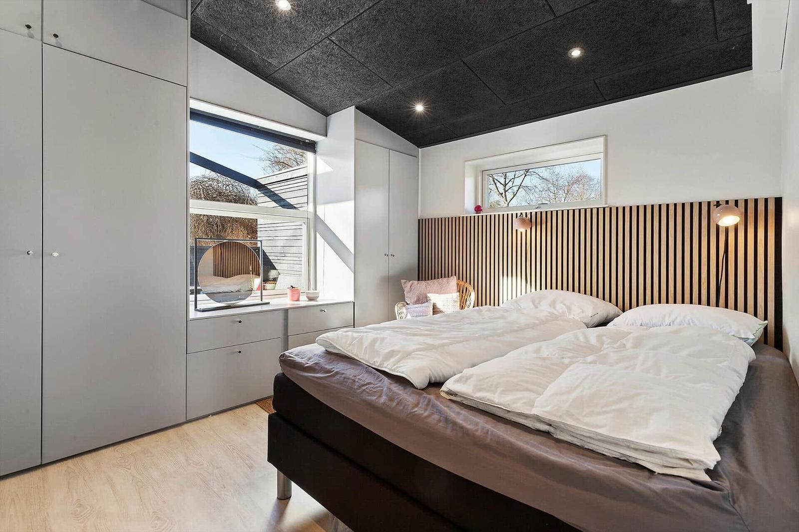 Schlafzimmer mit Doppelbett, Holzverkleidung, Fenster und Schränken.