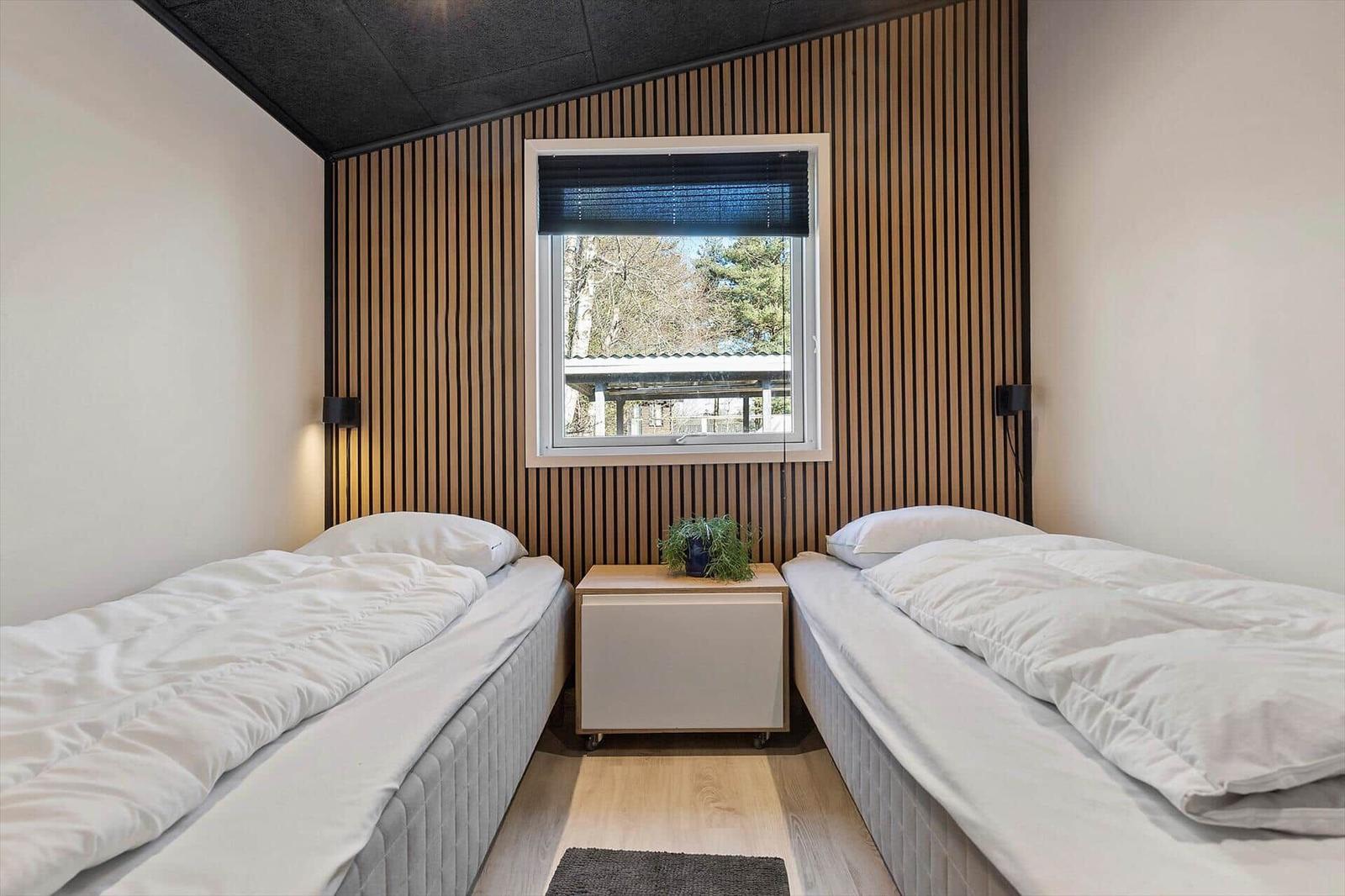 Zwei Betten mit weißer Bettwäsche stehen in einem Raum mit Holzwand und Fenster.