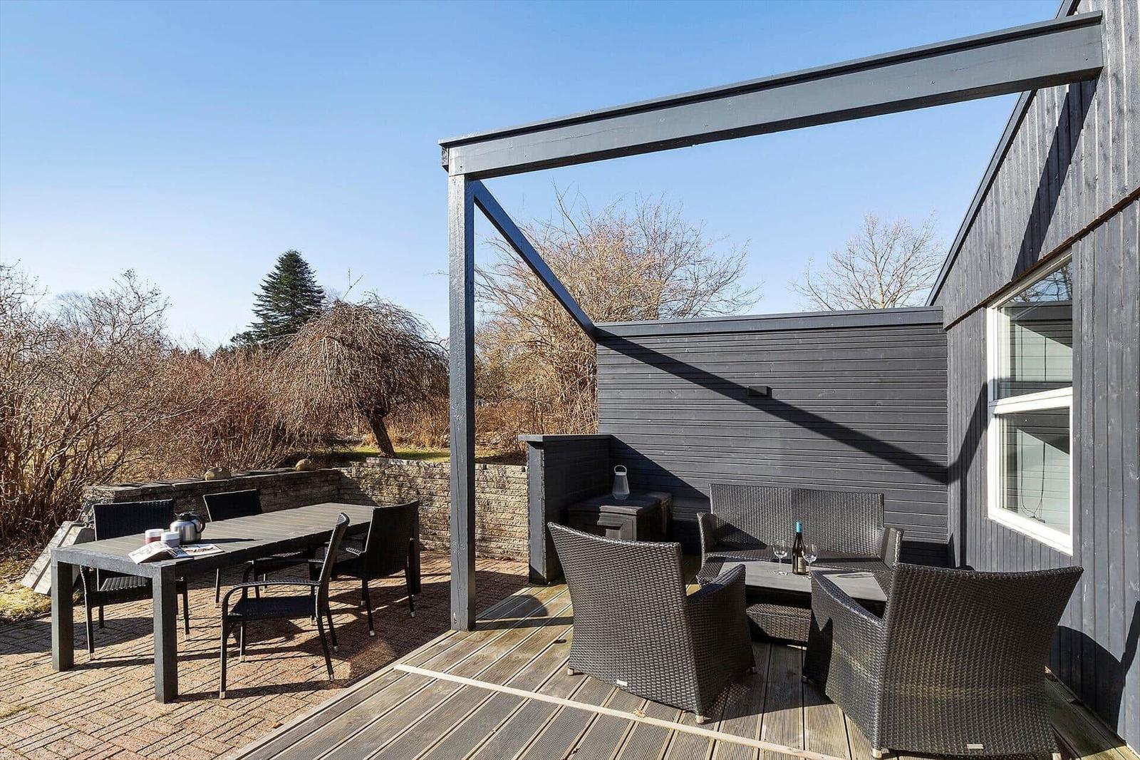 Terrasse mit Tisch, Stühlen und Sitzbereich unter Pavillon. Holzdecke und dunkle Wände.