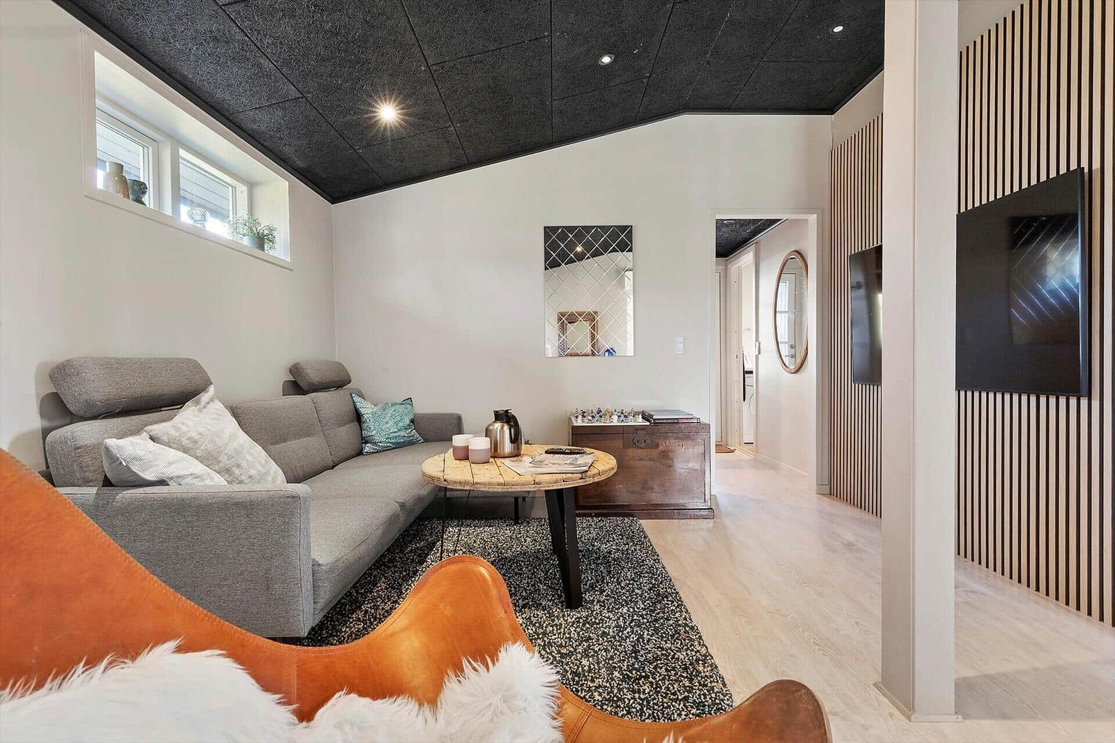 Wohnzimmer mit grafer Sofa, Holztisch und Fernseher an Holzwand.