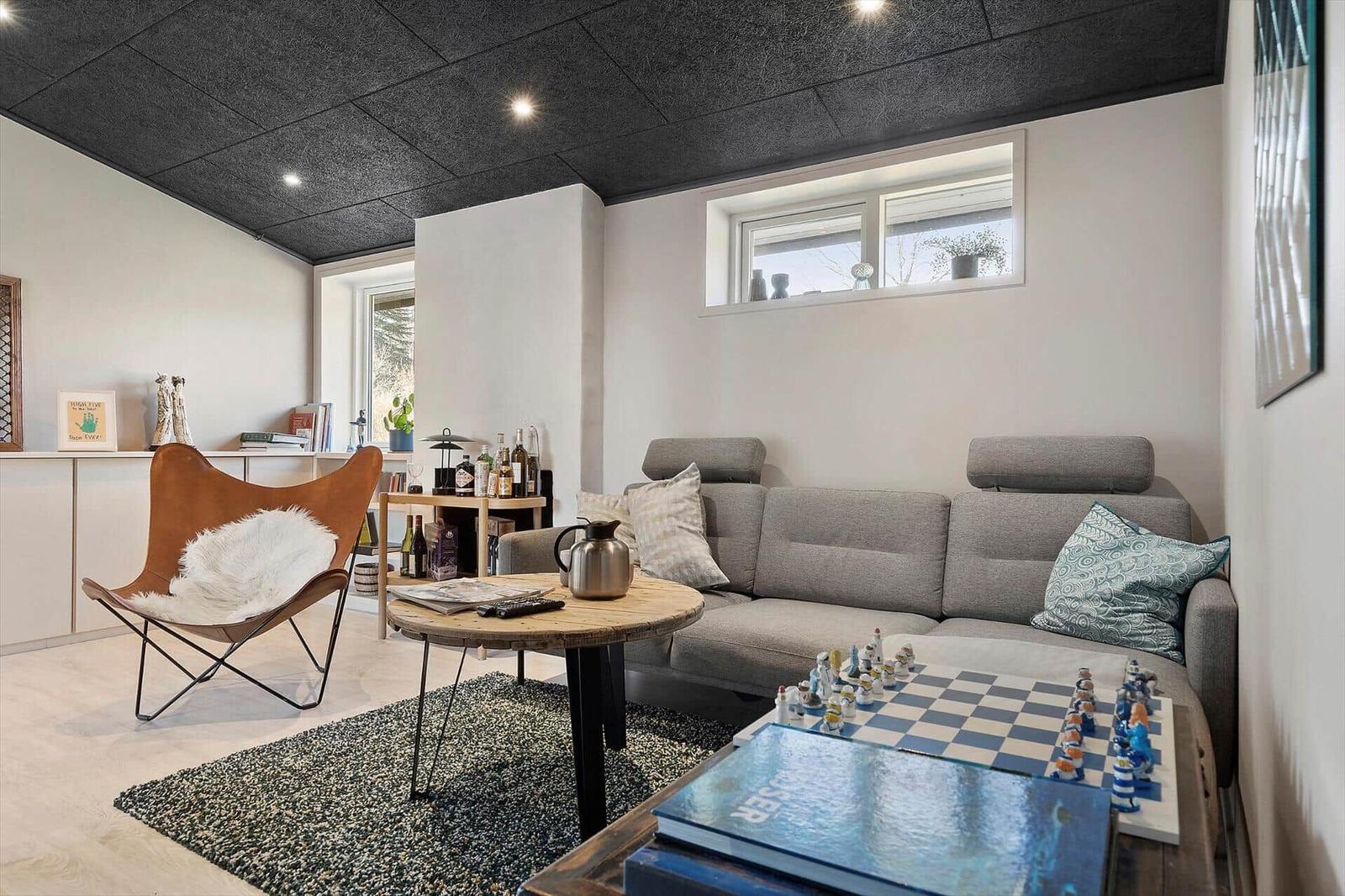 Wohnzimmer mit grauem Sofa, brauner Sessel und Schachspiel auf Tisch.