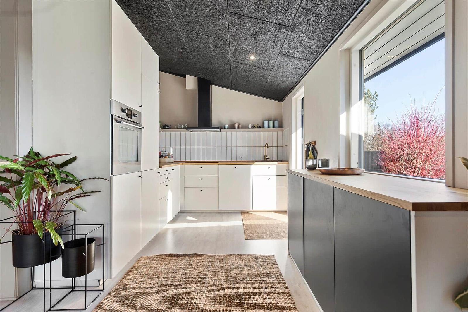 Moderne Küche mit weißen Schränken, Holzoberfläche und großem Fenster.