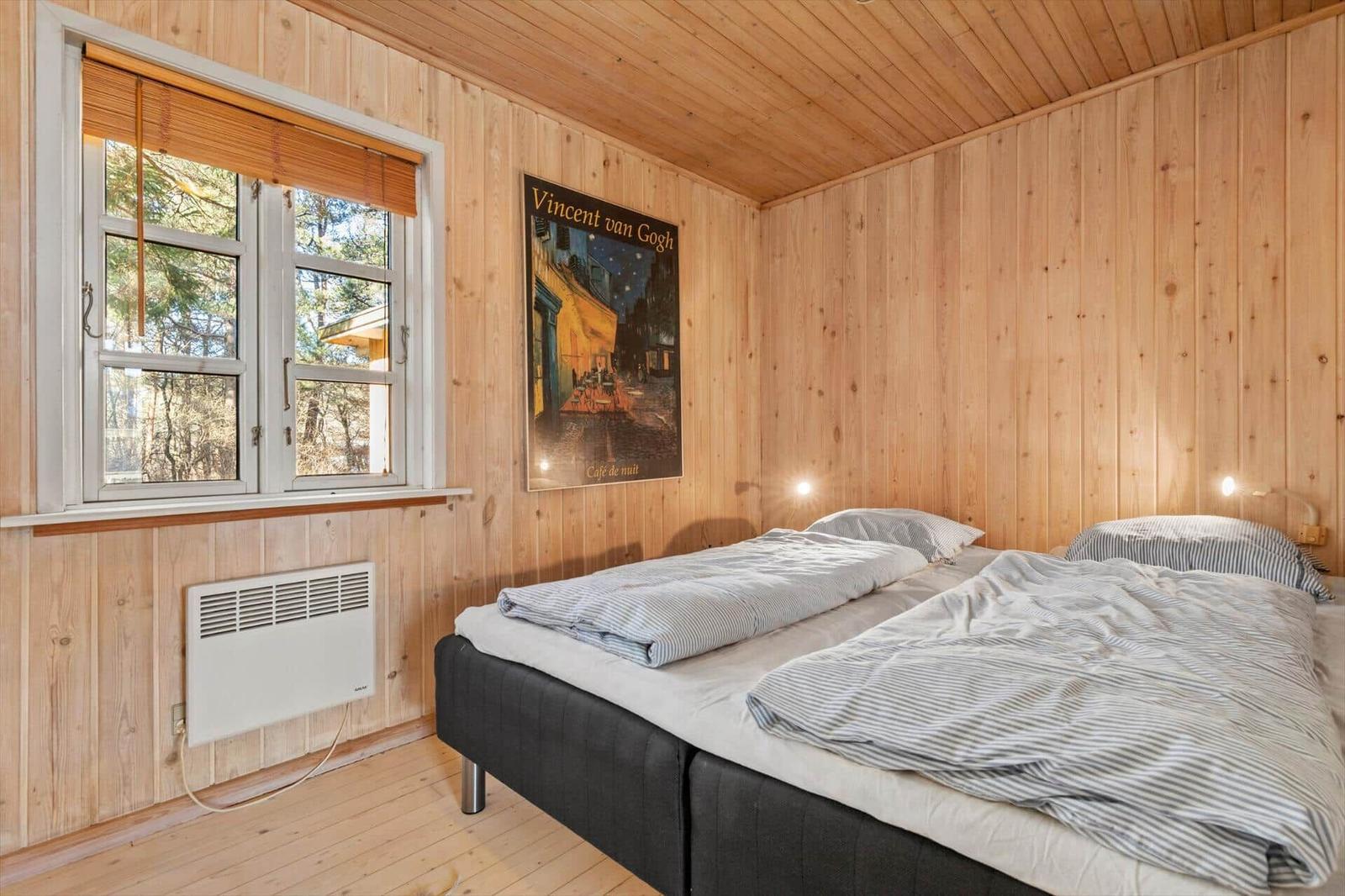 Schlafzimmer mit Holzwand, Bett und Fenster mit Blick auf Wald.