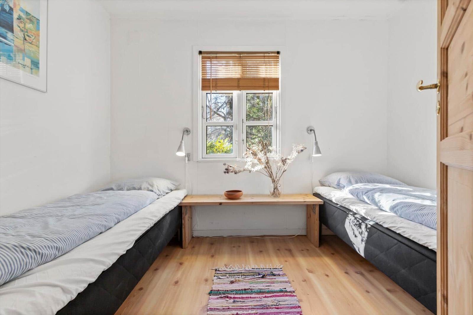 Zwei Betten stehen in einem Raum mit Holzboden und Fenster. Zwischen ihnen steht ein Tisch mit Blumen.