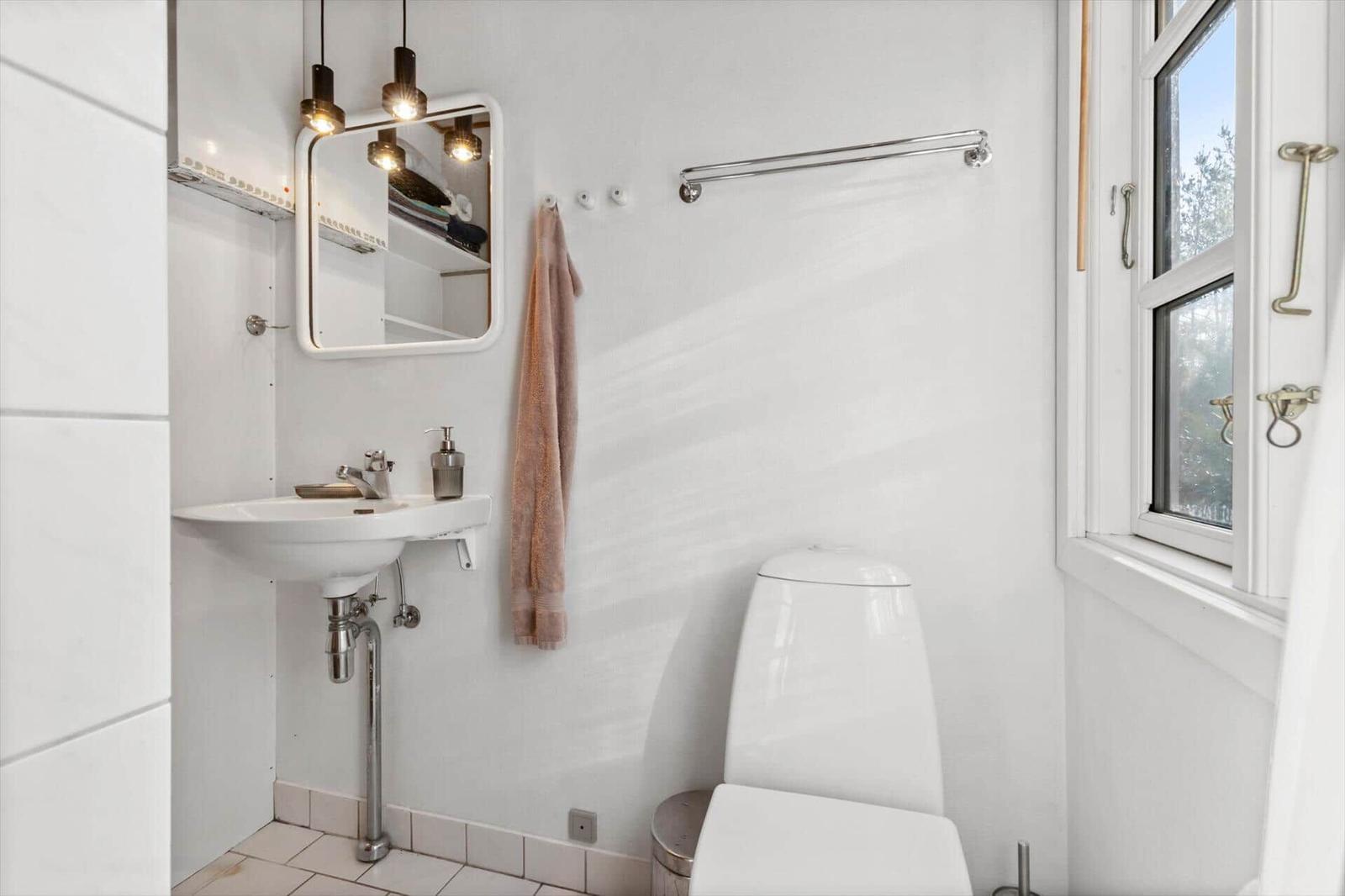 Badezimmer mit Waschbecken, Spiegel und Toilette. Fenster mit Blick nach draußen.