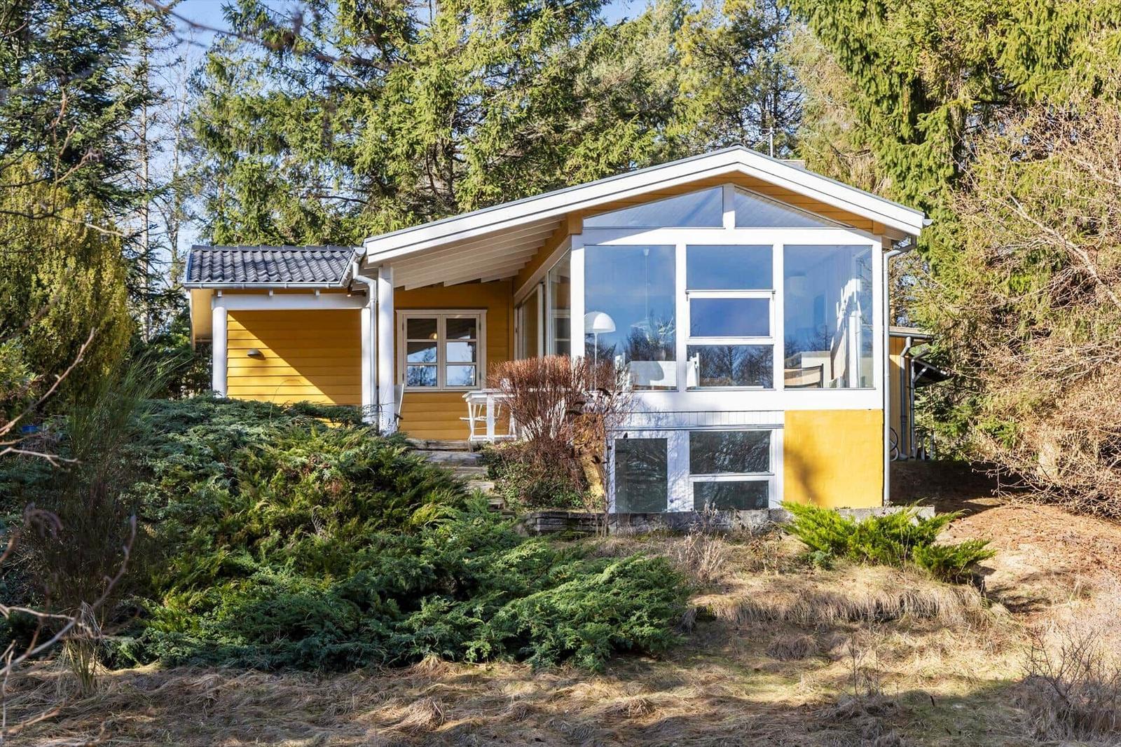 Ein gelbes Haus mit großem Glasbereich und Terrasse im Wald