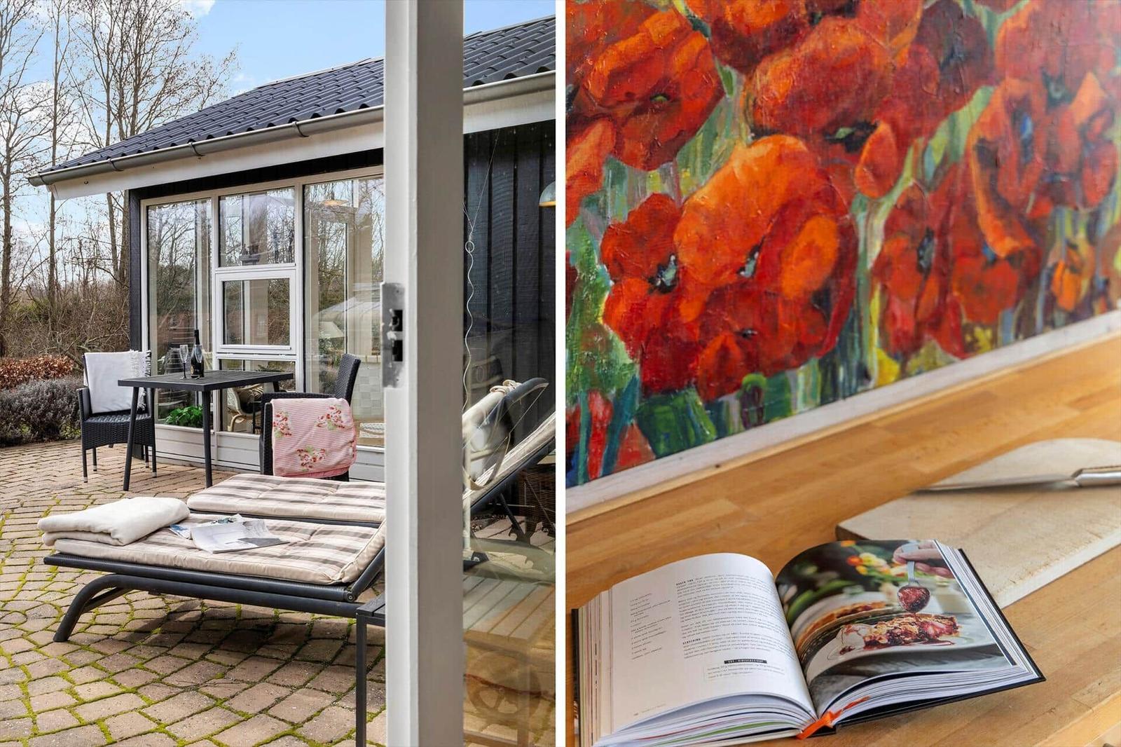 Terrasse mit Liege und Tisch. Innen: Wandbild mit Mohnblumen und offenes Kochbuch.