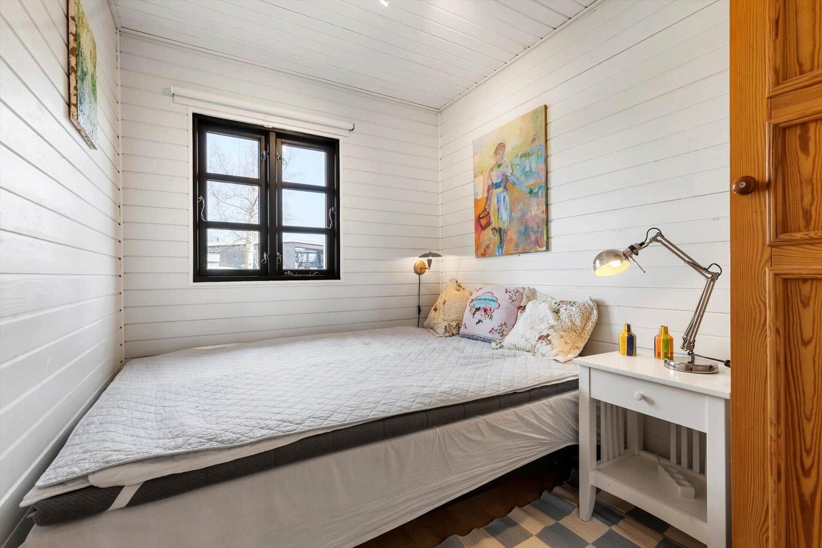 Schlafzimmer mit Bett, Nachttisch und Fenster. Wände sind weiß verputzt.